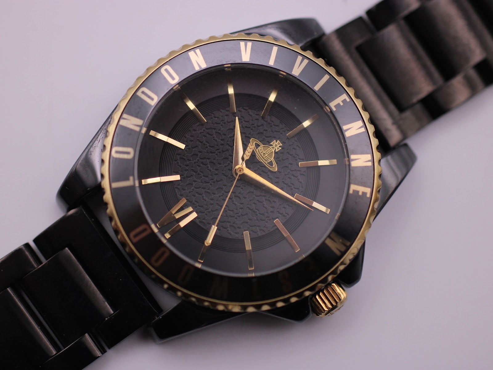 Close-up front view of the black textured dial with gold-tone baton indices, Roman numeral VI, and Vivienne Westwood orb logo.