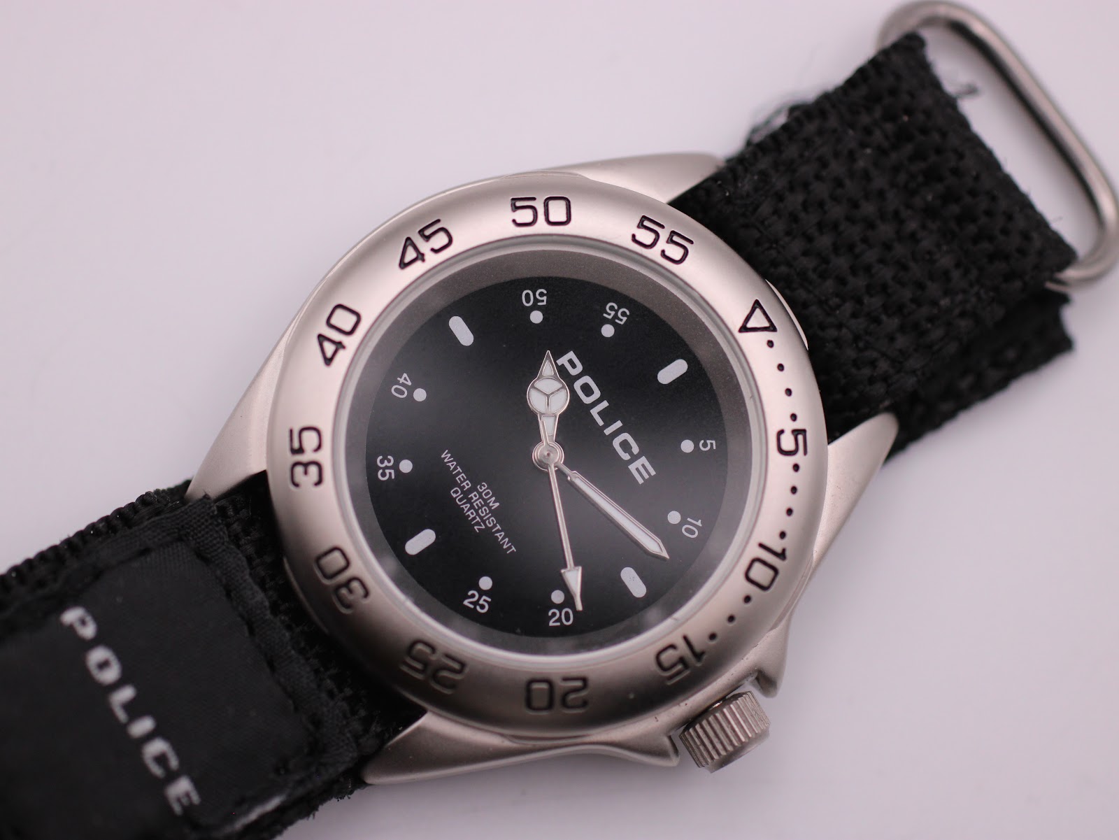 Close-up, slightly angled view of the Police watch dial, silver bezel, and the texture of the black fabric strap.