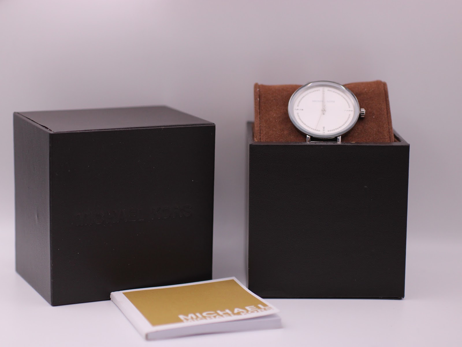 Michael Kors watch displayed with its original dark brown box and accompanying papers, confirming inclusions.