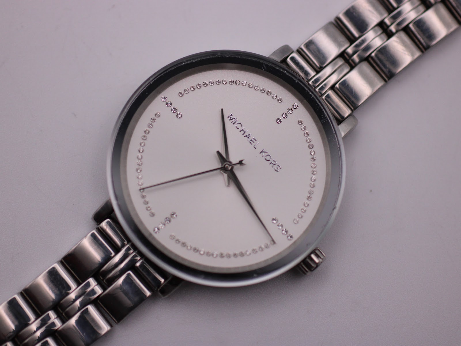 Close-up, slightly angled view of the Michael Kors white dial, showing the crystal minute track and branding.