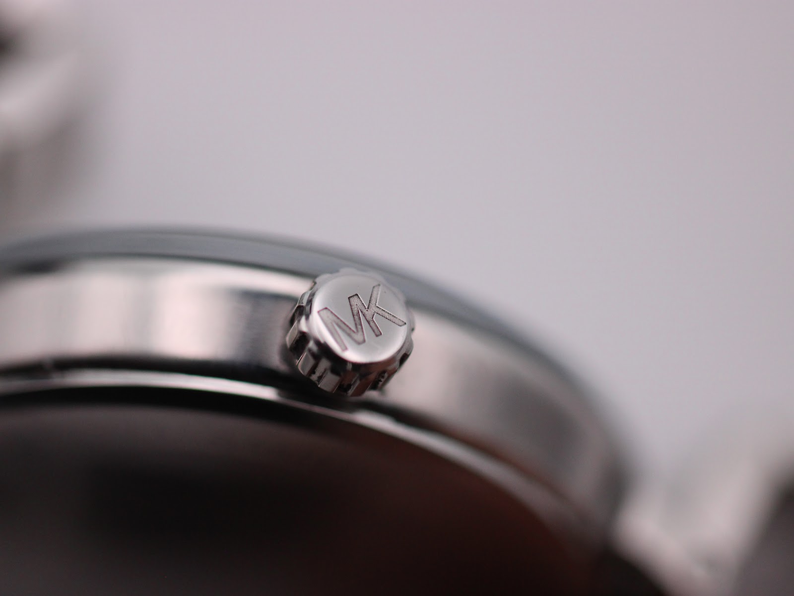 Extreme close-up of the textured, signed 'MK' crown on the side of the watch case.