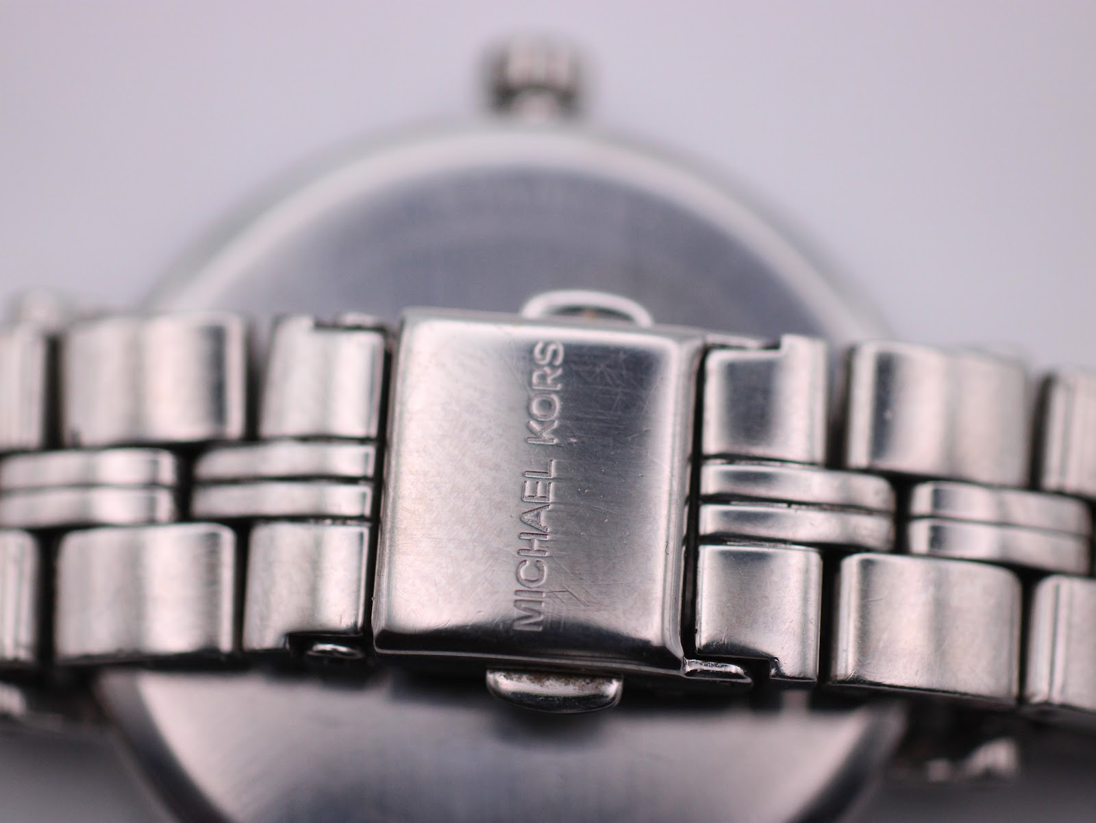 Close-up view of the signed 'MICHAEL KORS' fold-over clasp on the stainless steel bracelet.