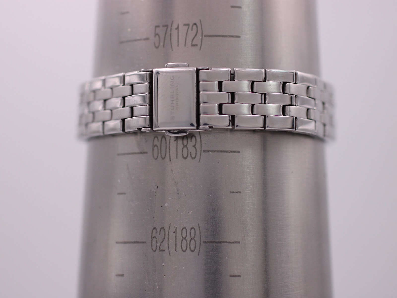 Close-up of the Stührling Original stainless steel bracelet and signed clasp on a wrist sizing gauge, showing a circumference of approximately 18.3 cm.