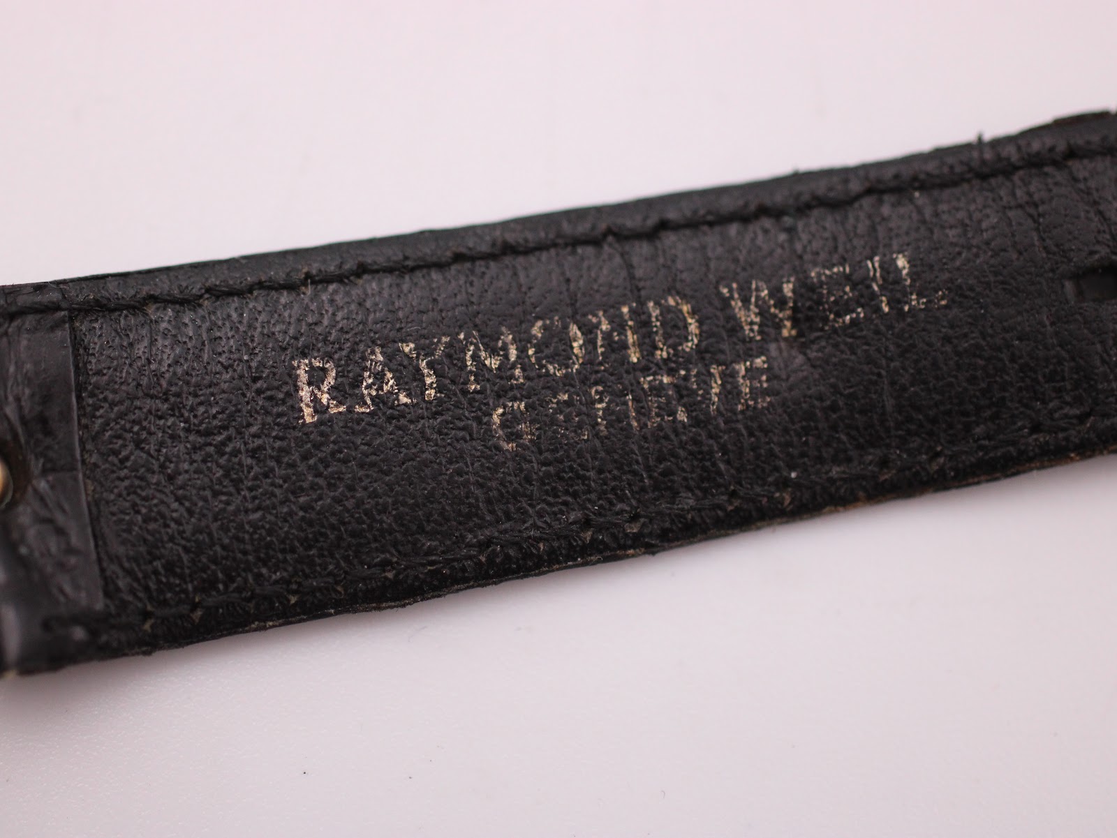 Close-up of the underside of the black leather strap showing 'RAYMOND WEIL GENEVE' stamping.