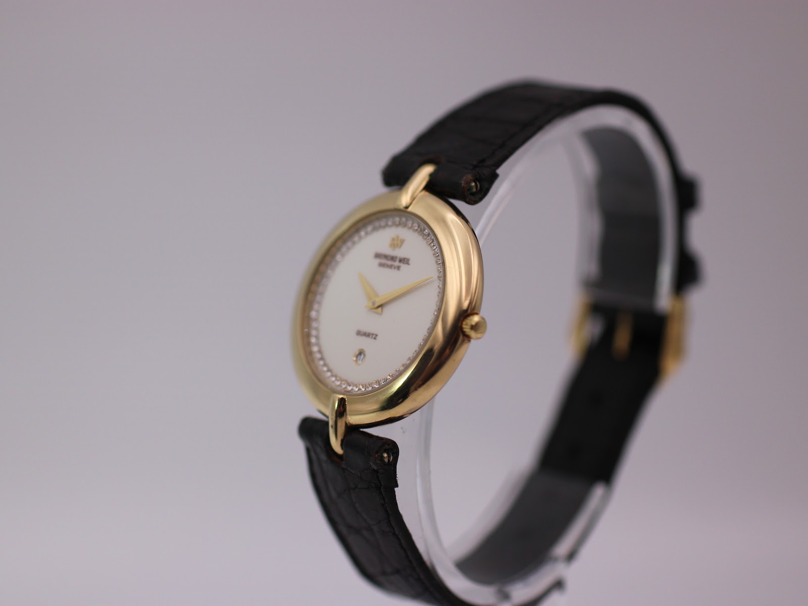Angled three-quarter view of Raymond Weil 5350 watch on display stand, highlighting the gold case and black leather strap.