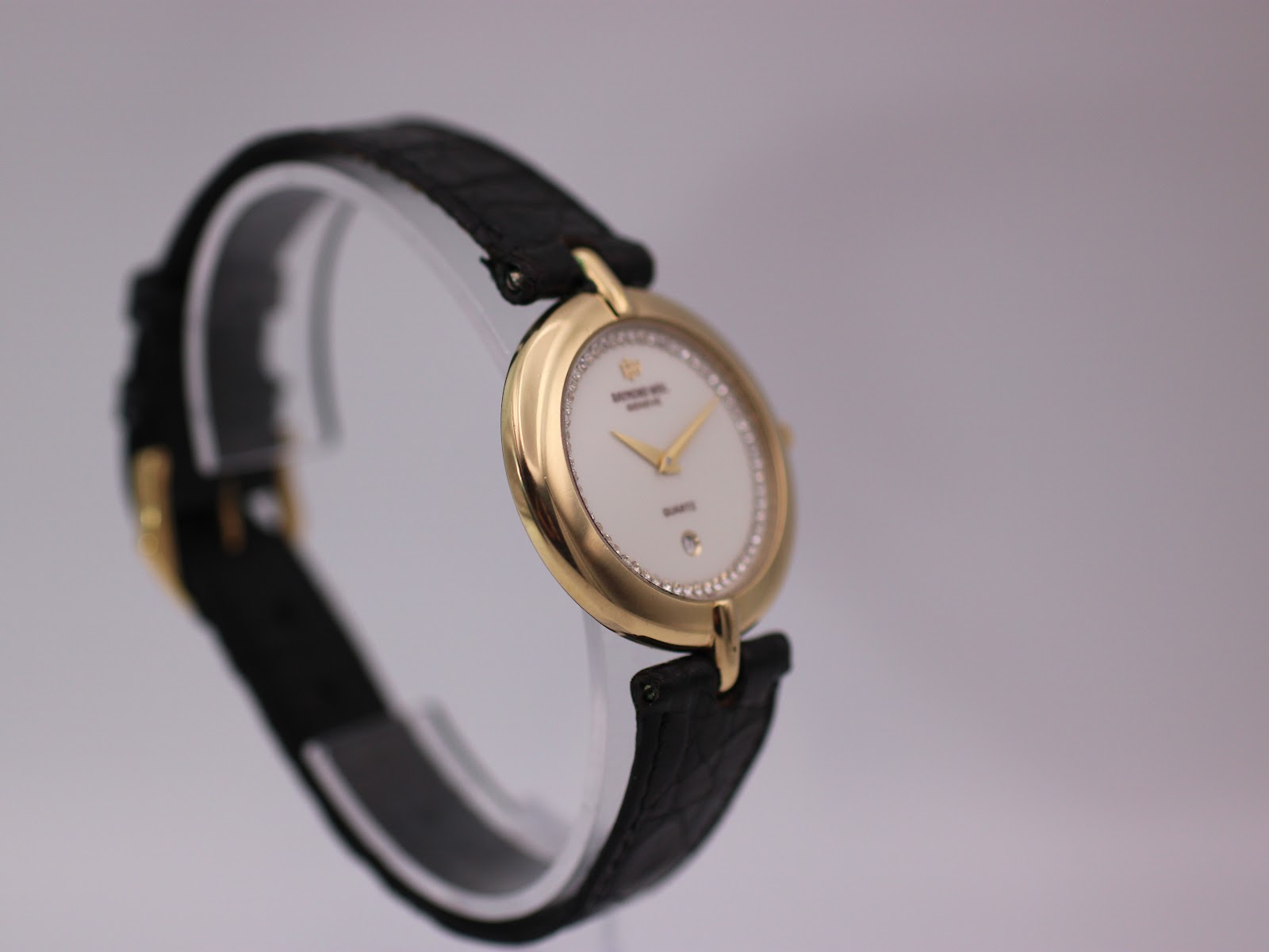 Side view of Raymond Weil 5350 watch on display stand, showcasing the gold case profile and crown.