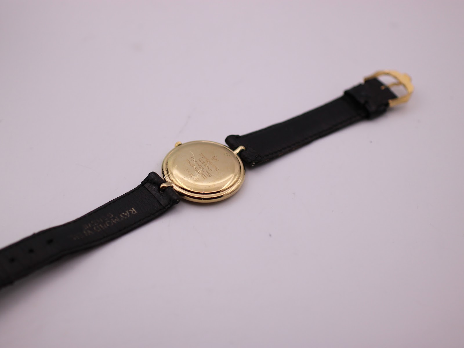 View of the watch from the back, showing the gold case back and the full black leather strap with buckle.