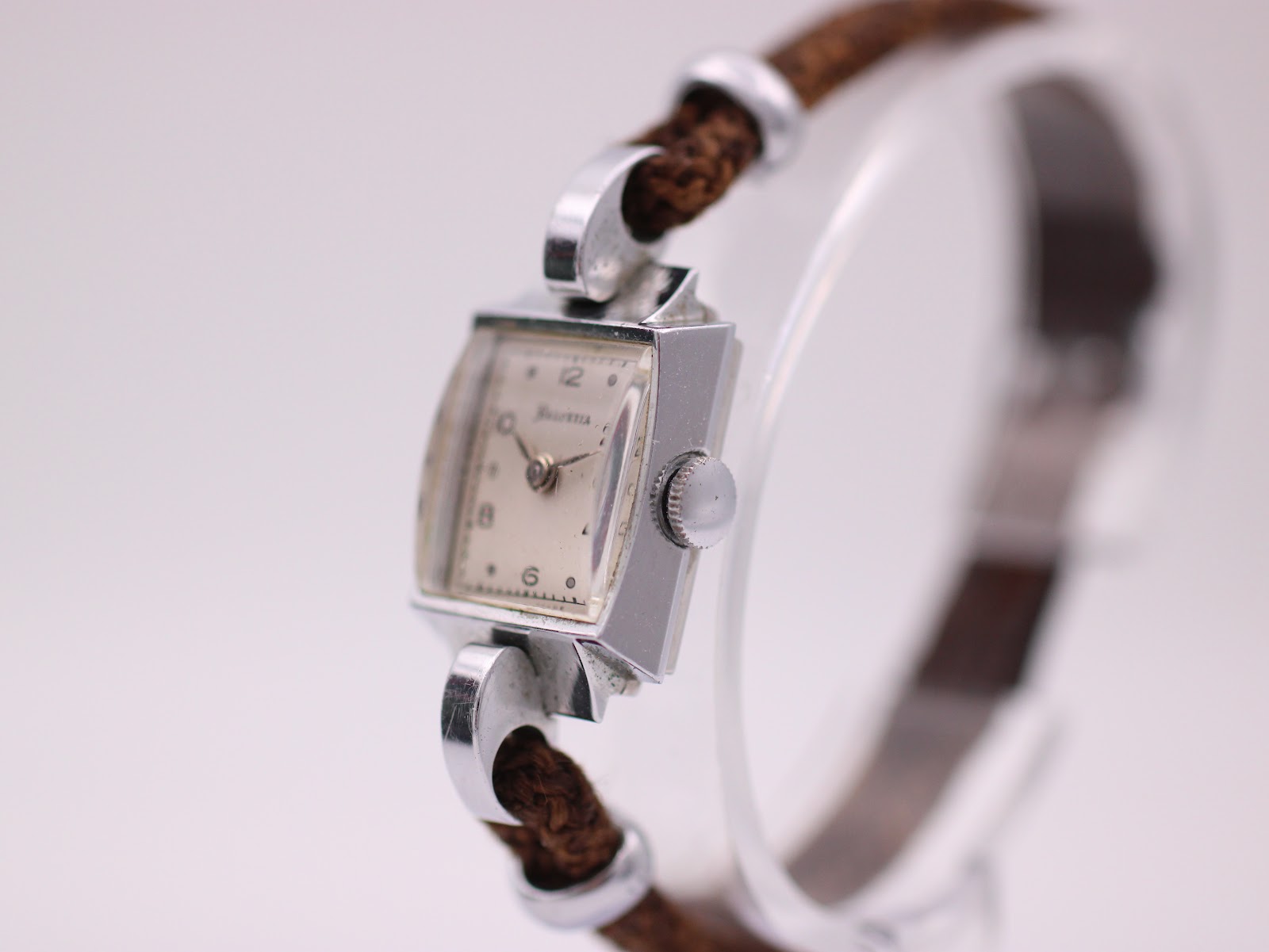Angled perspective of the Helvetia watch, highlighting the side of the silver case, the crown, and the texture of the brown fabric strap.