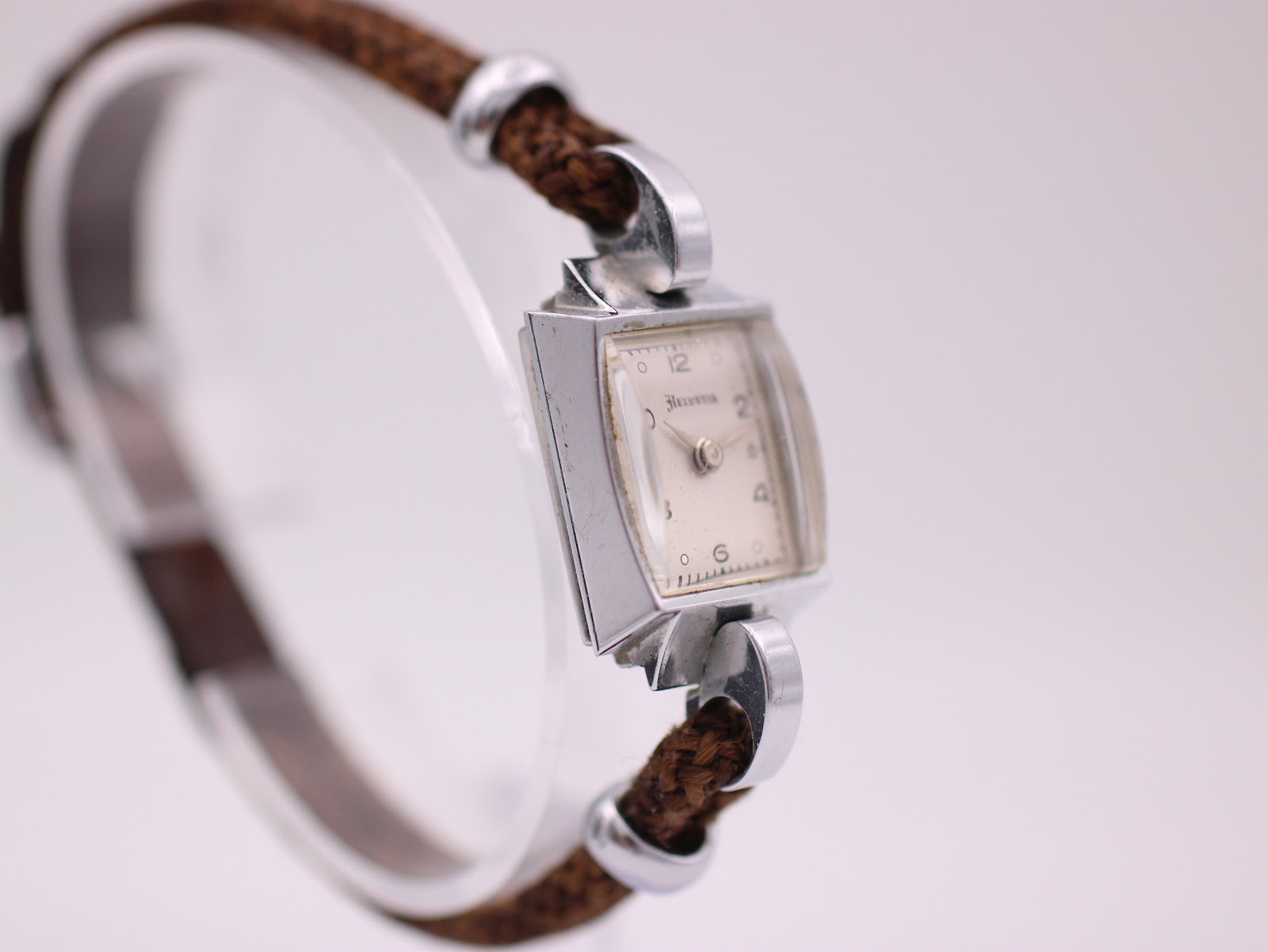 Three-quarter view of the Helvetia watch, showcasing the dial, the profile of the rectangular case, and the integrated fabric strap design.