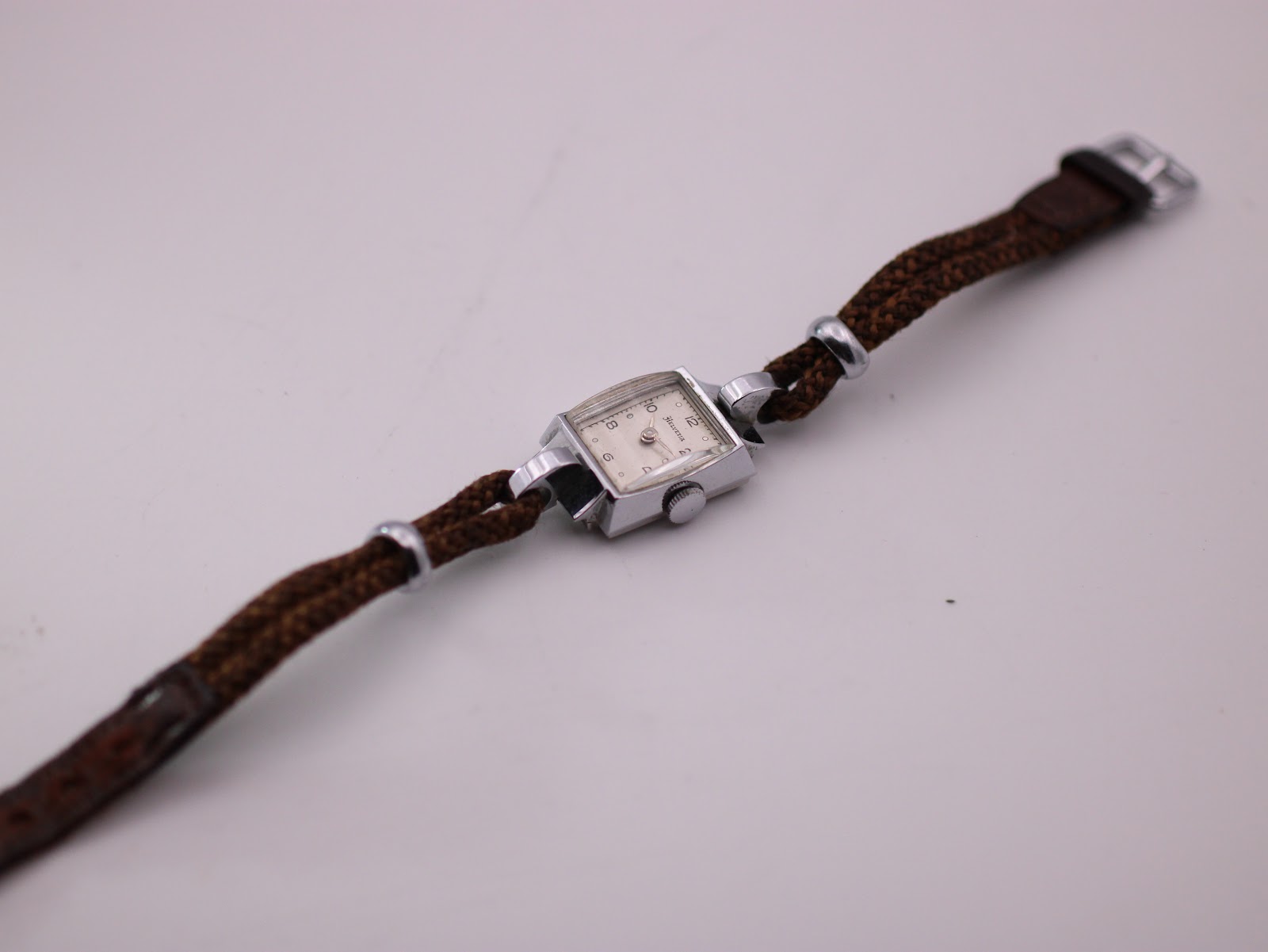 Overhead angled shot of the full Helvetia watch, displaying the rectangular case and the length of the brown woven fabric strap with its buckle.