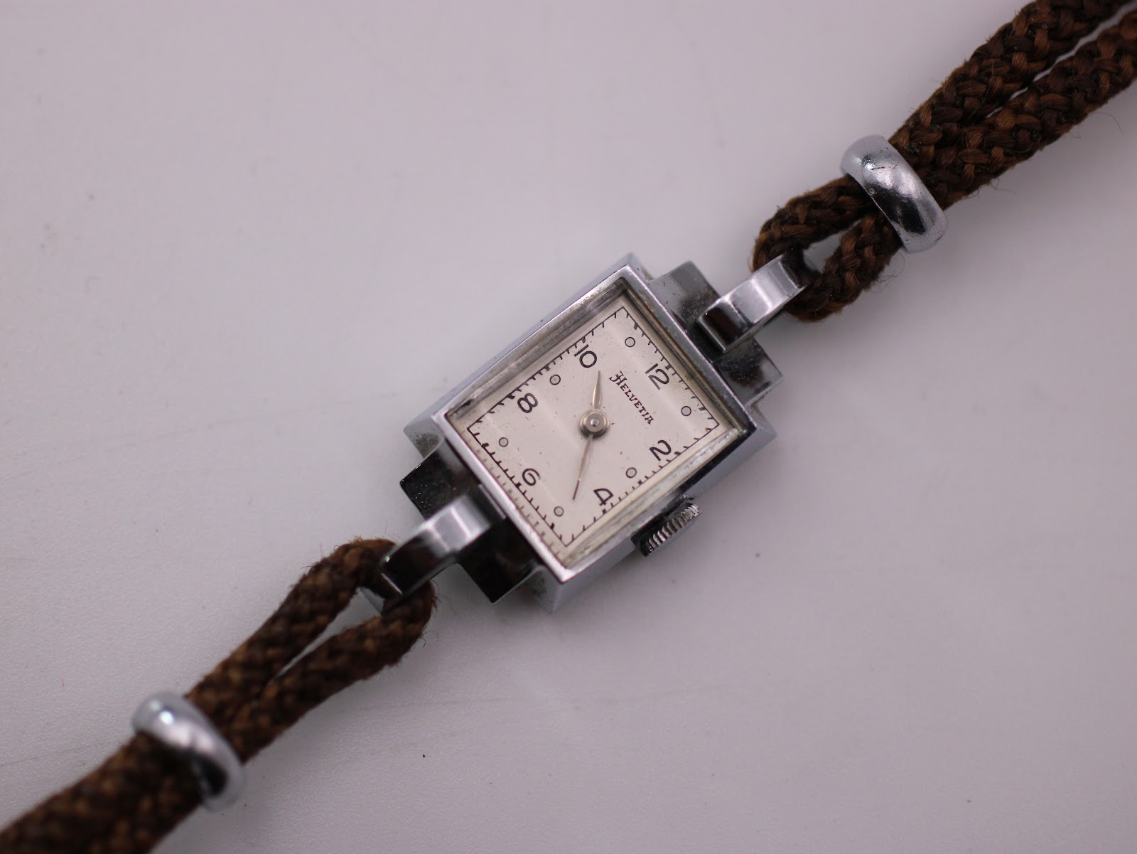 Close-up, slightly angled shot of the Helvetia watch's cream dial, Arabic numerals, and a segment of the brown fabric strap.