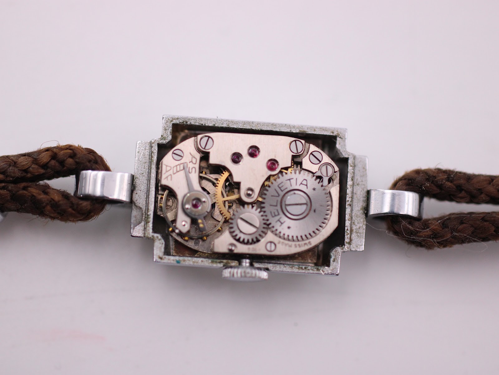 Close-up of the Helvetia manual wind movement, visible within the open rectangular case, showing the intricate gears and ruby jewels.