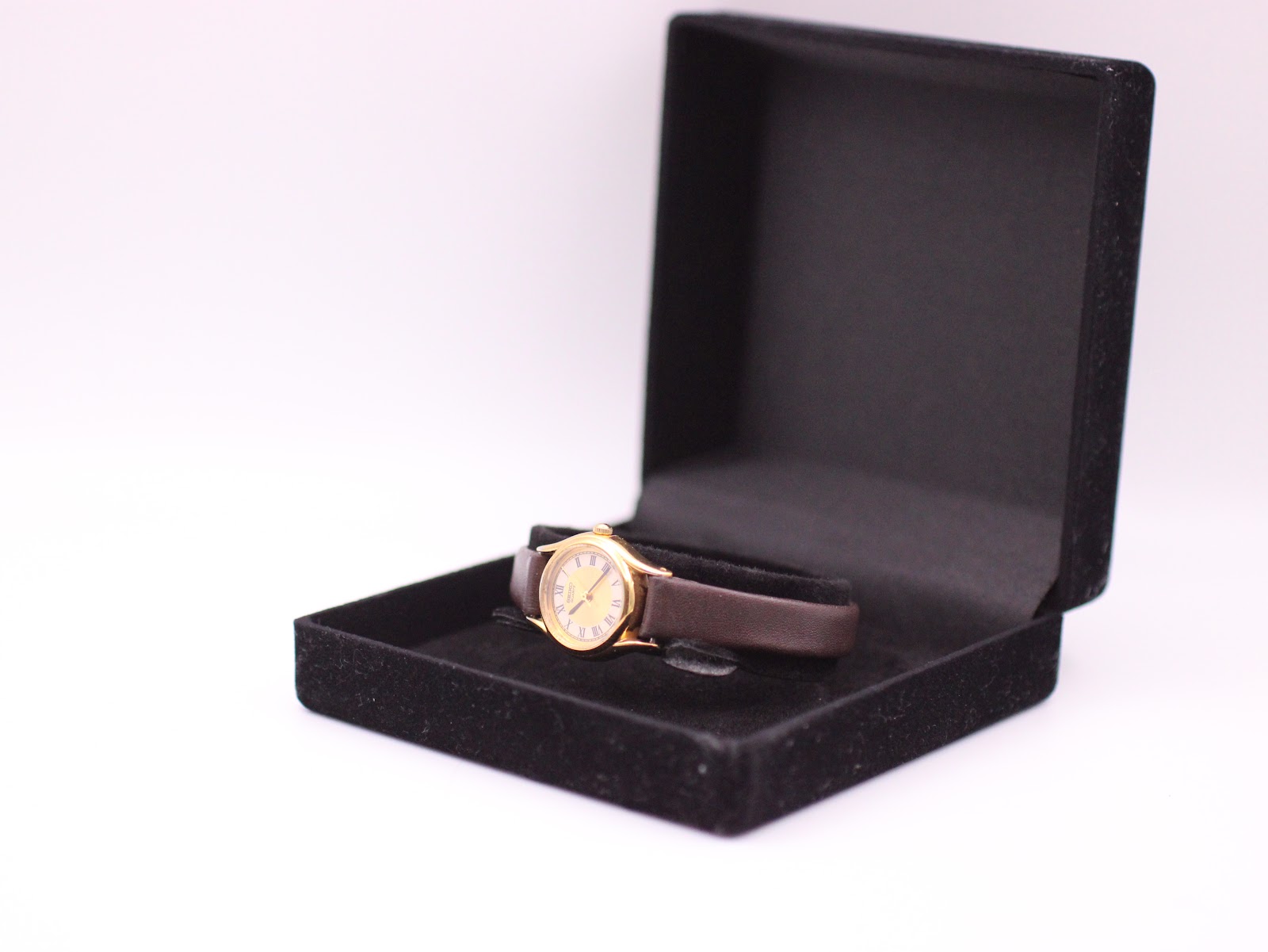 The Seiko watch displayed in a black velvet presentation box, resting on its brown leather strap.