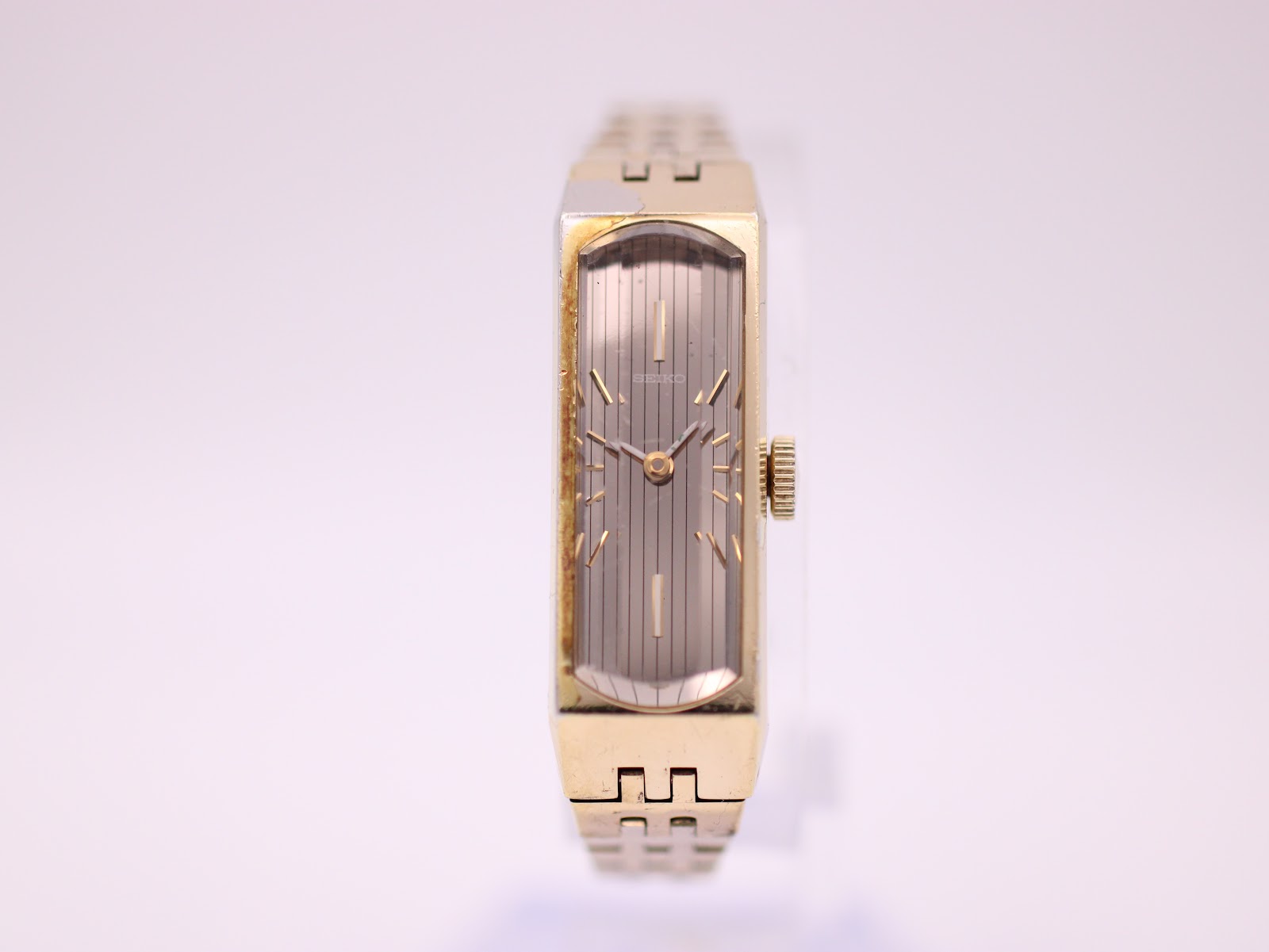Front view of gold tone Seiko rectangular watch with silver textured dial and gold baton indices.