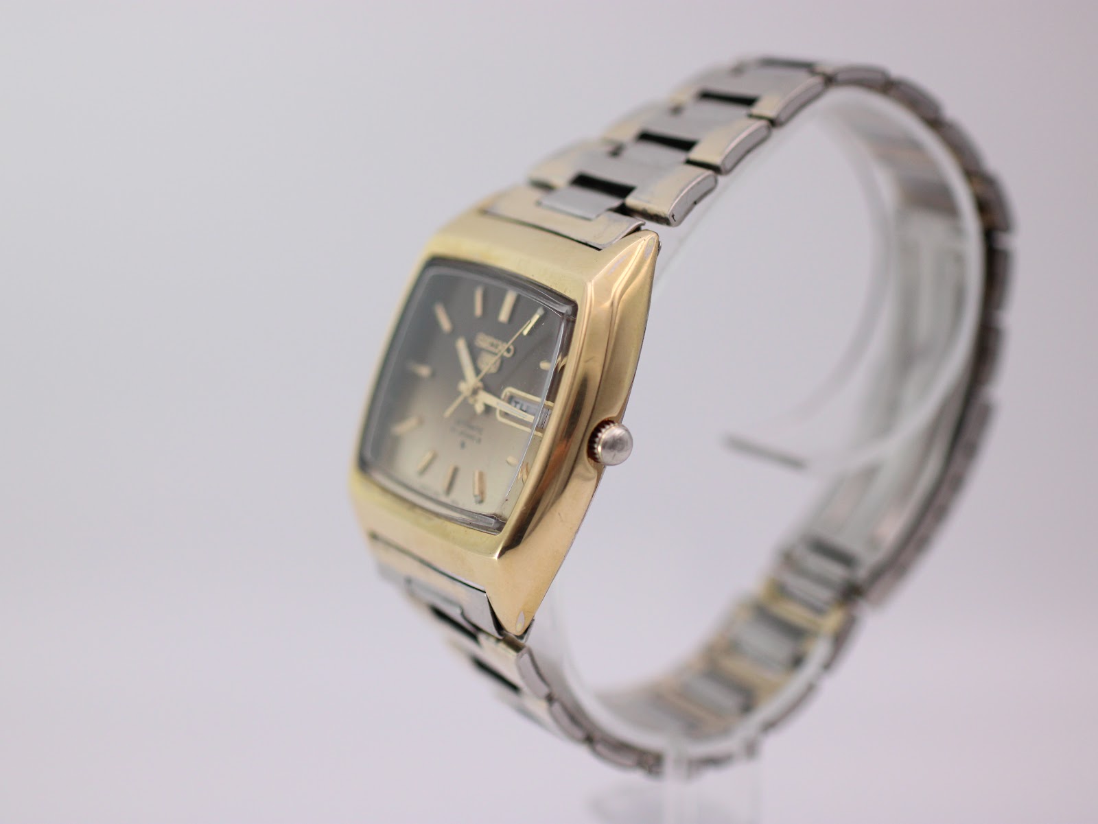 Angled side view of the Seiko watch on a clear stand, showing the curved case profile and bracelet.