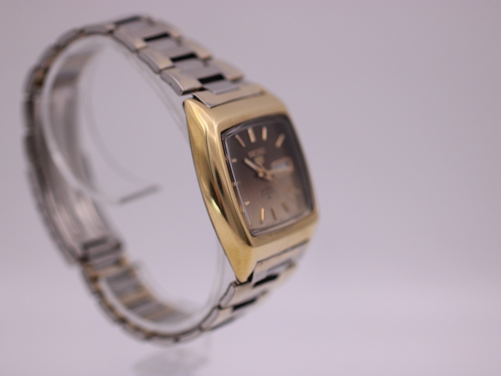 Another angled view of the Seiko watch on a clear stand, highlighting the gold-plated case from a different perspective.
