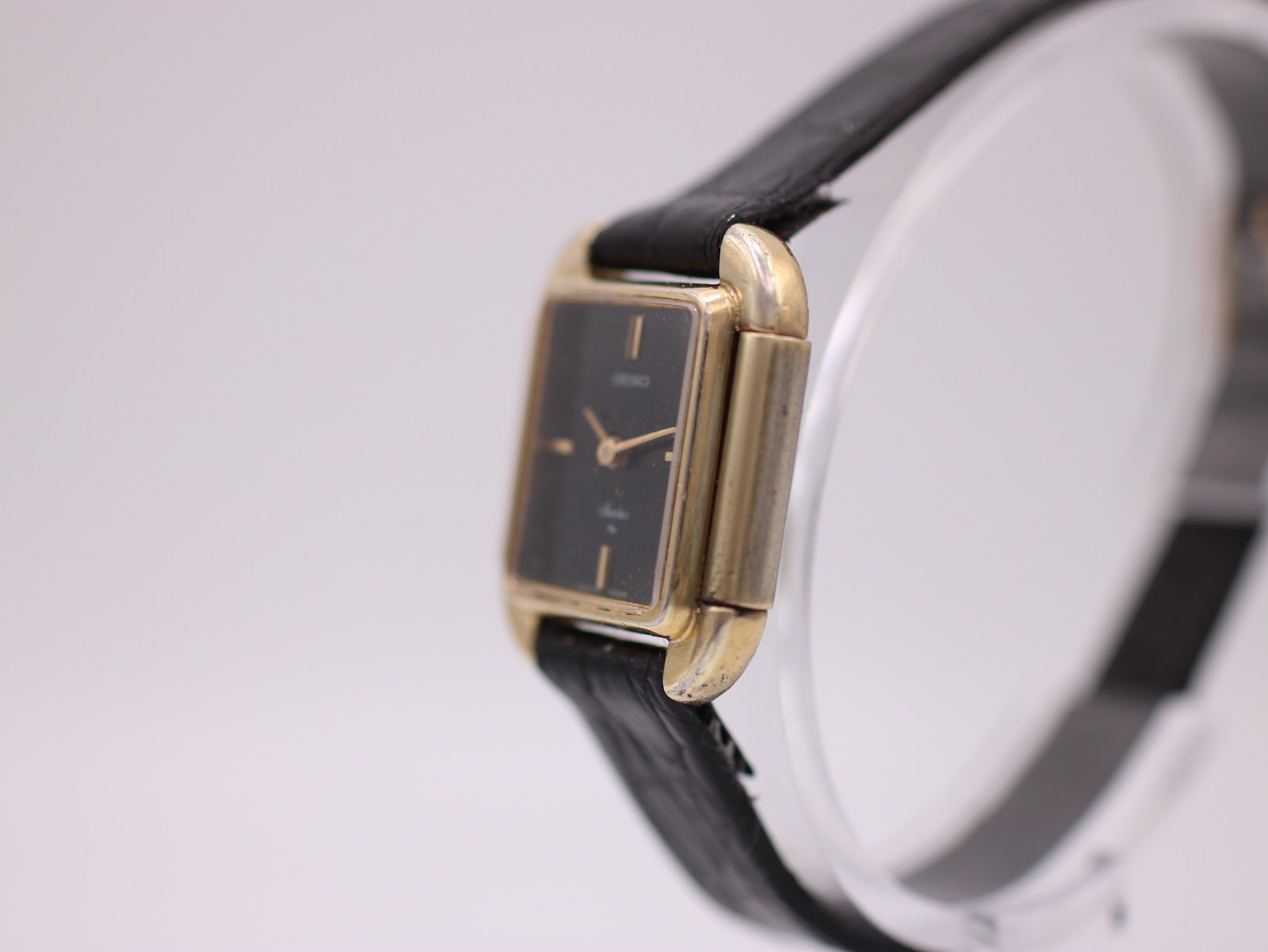 Side profile view of the gold-plated Seiko Socie watch, showing the rectangular case and crown on a display stand.
