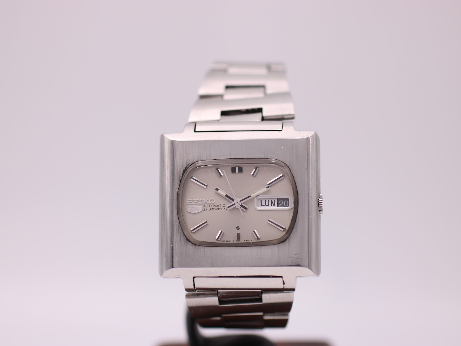 Front view of vintage Seiko 6119-5401 automatic watch with square stainless steel case and cream cushion dial, on stand.
