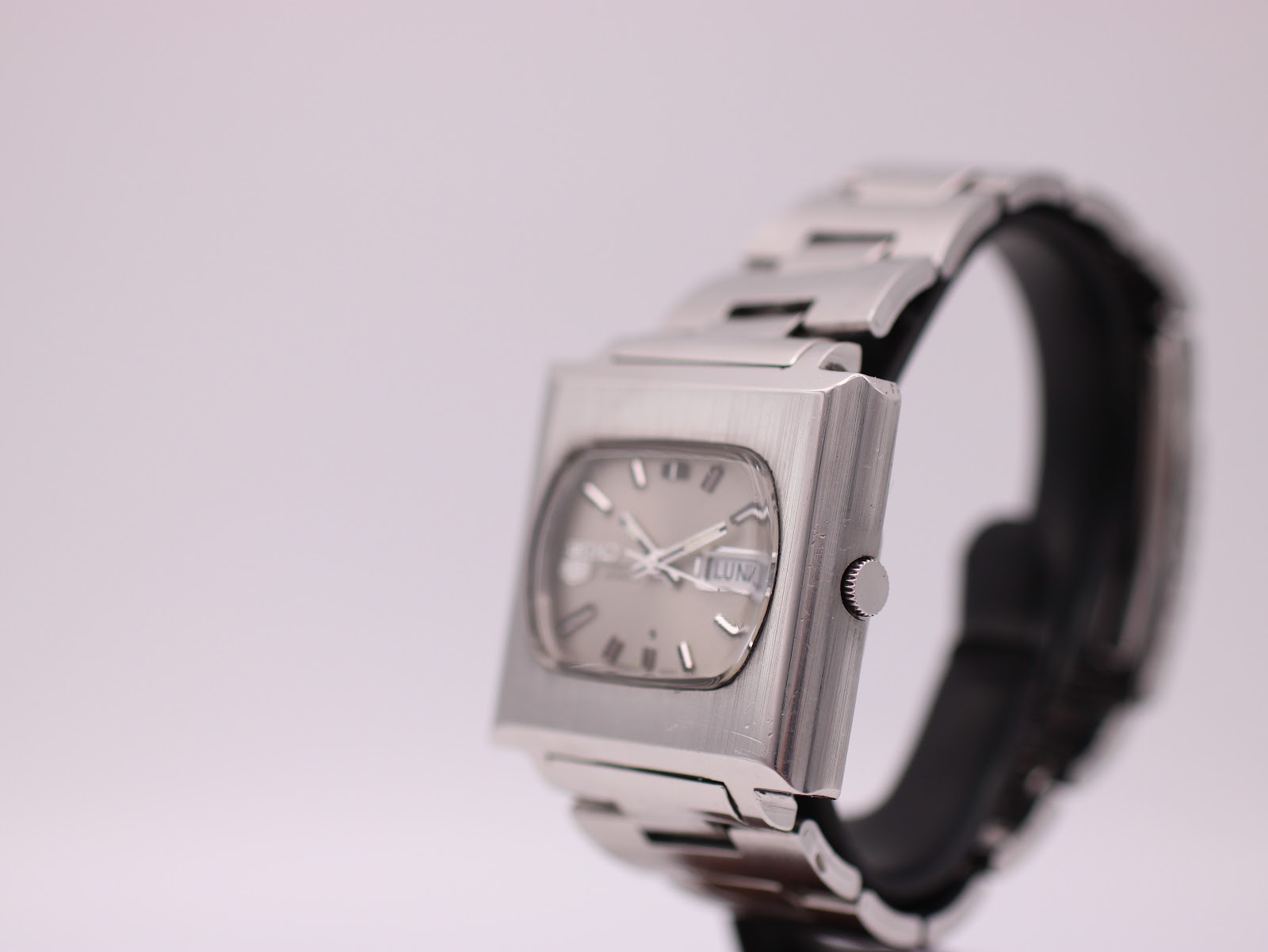 Angled side view of vintage Seiko 6119-5401 showing crown and brushed case finish, on stand.