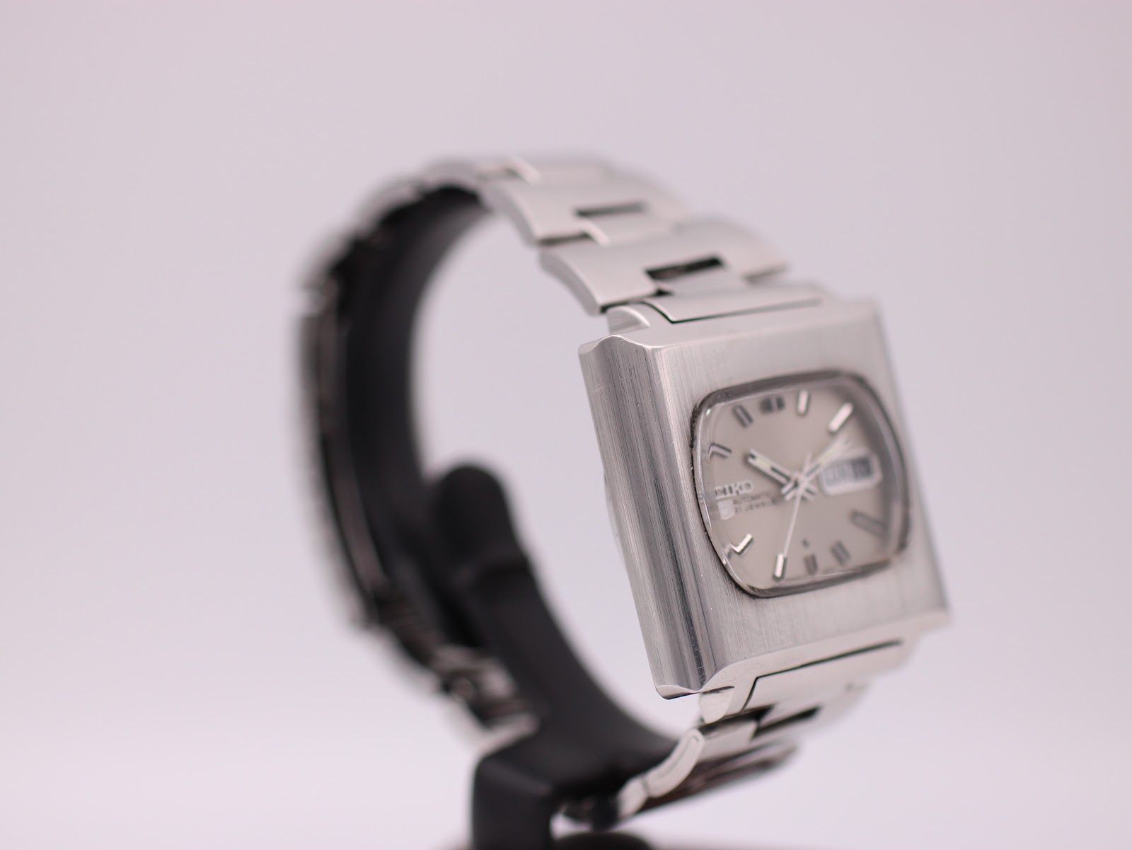 Opposite angled side view of vintage Seiko 6119-5401 showing case lines and integrated bracelet, on stand.