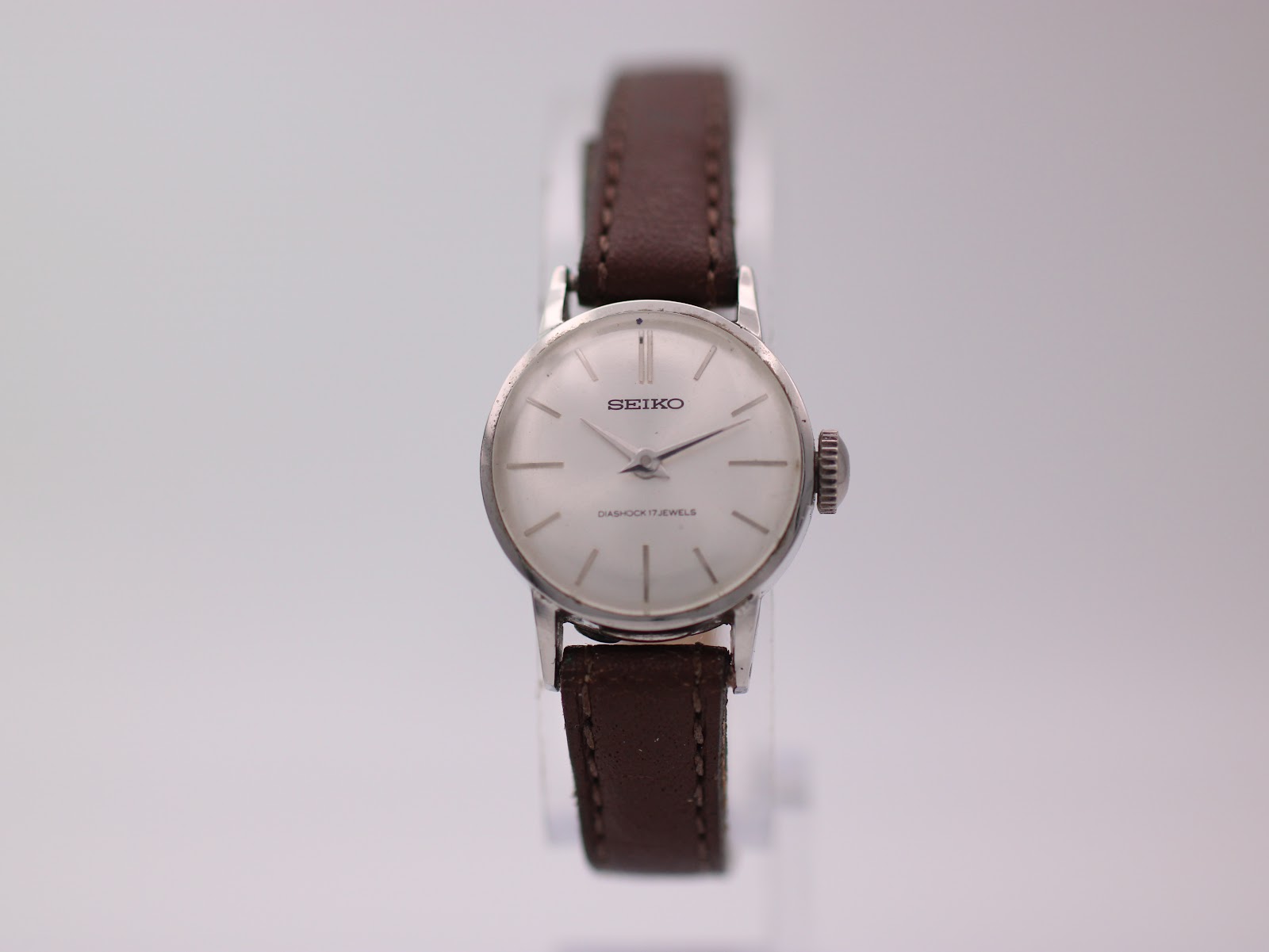 Front view of vintage Seiko 21-0030 ladies' watch with silver sunburst dial and brown leather strap on a watch stand.