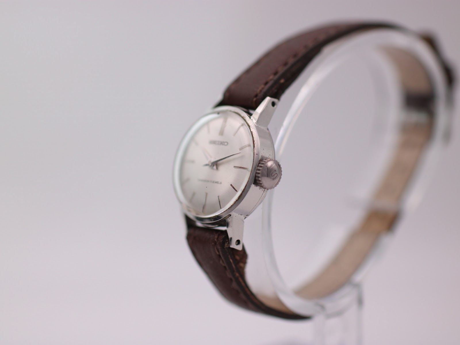 Angled side view of the Seiko watch, showing the crown and slender case profile on a watch stand.