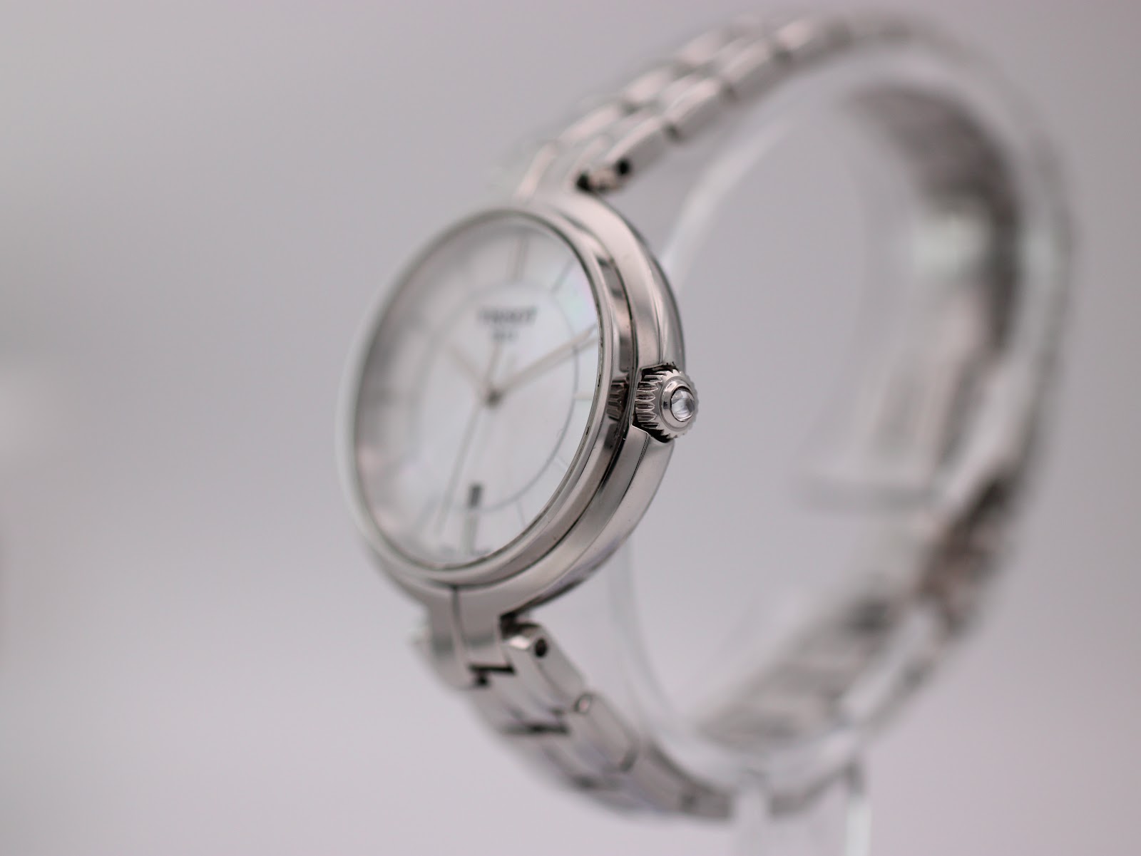 Side view of the Tissot watch showing the polished stainless steel case and fluted crown on a clear display stand.