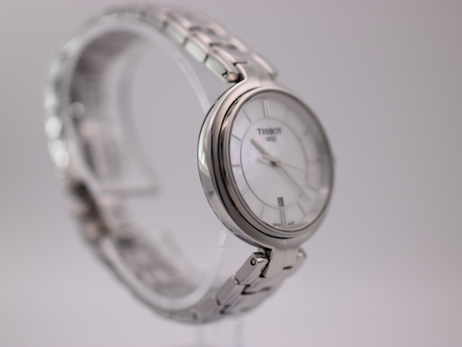 Angled side view of the Tissot watch on a display stand, highlighting the curved case and bracelet links.