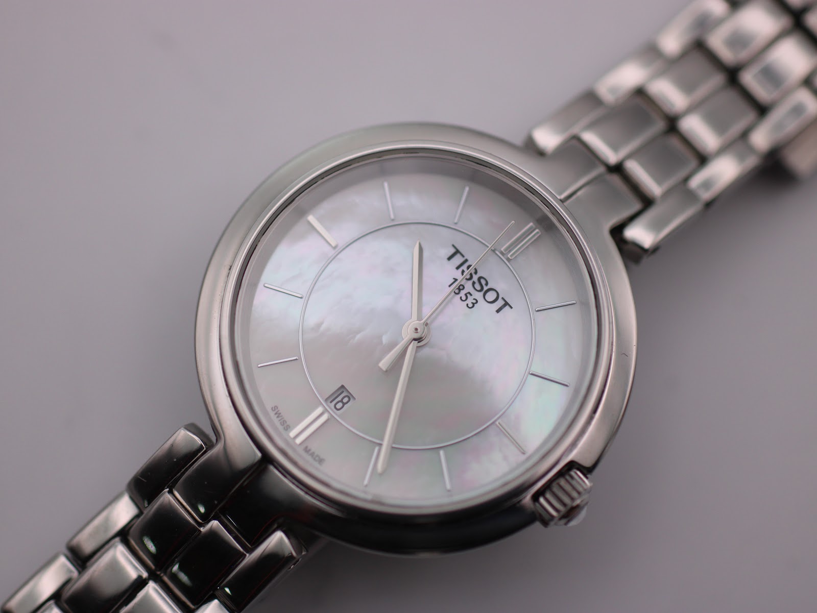 Close-up top-down view of the Tissot watch dial, revealing the iridescent mother-of-pearl texture, baton indices, and date window.