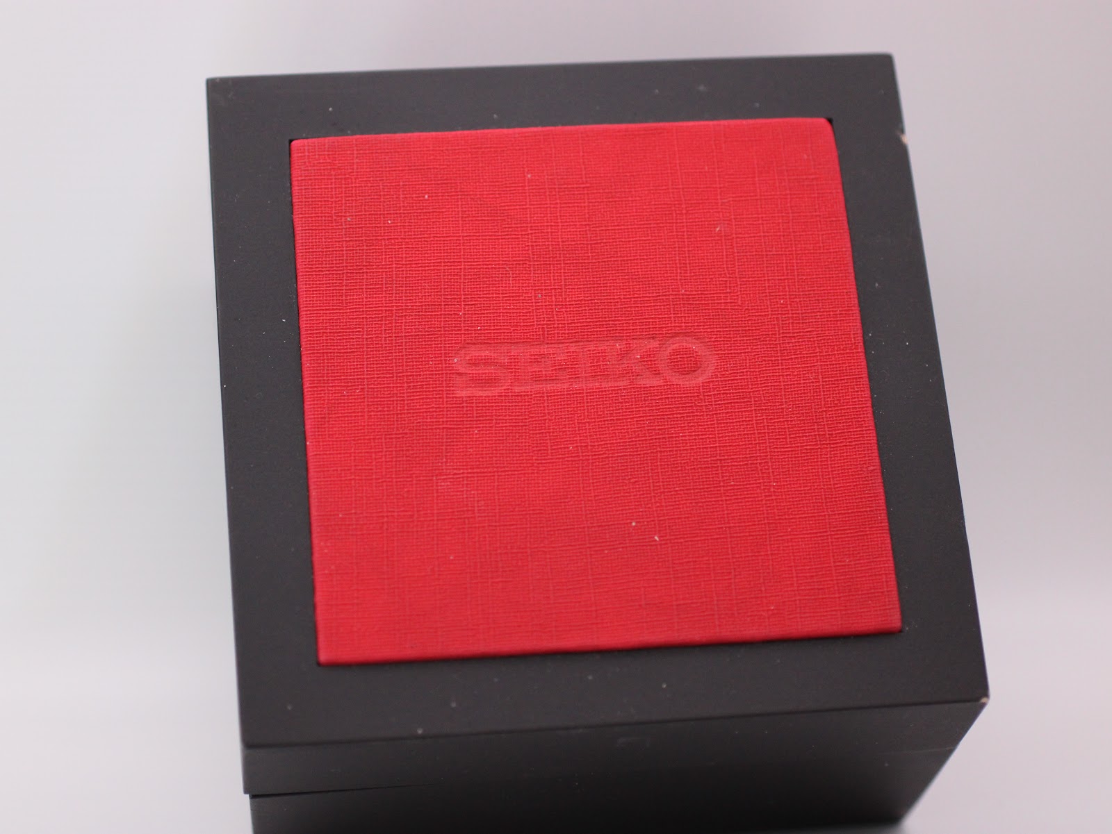 Top view of the closed generic black display box with a red textured lid, showing the word 'SEIKO' embossed on it.