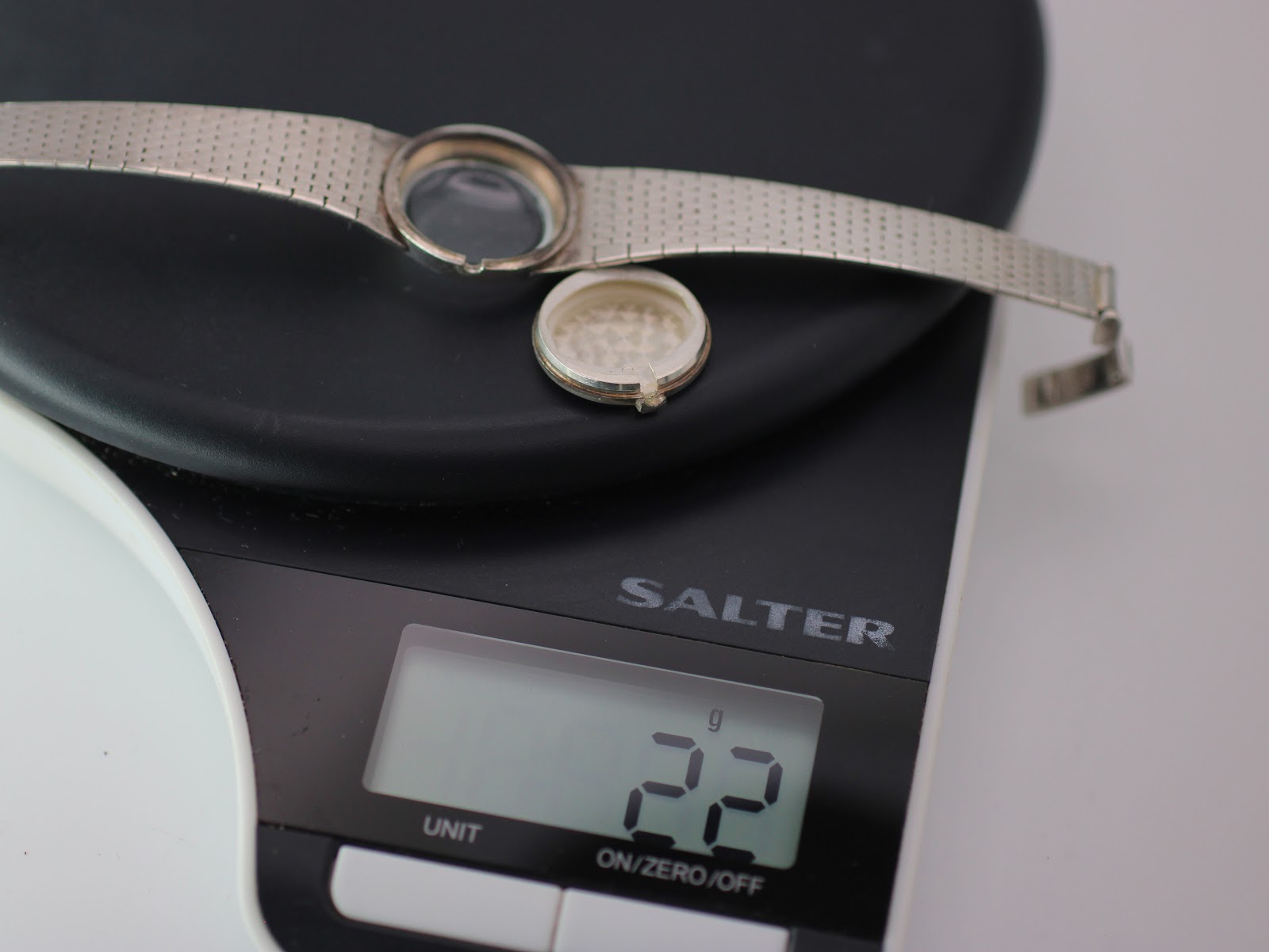 Watch case and case back resting on a digital scale, showing a weight of '22g'.