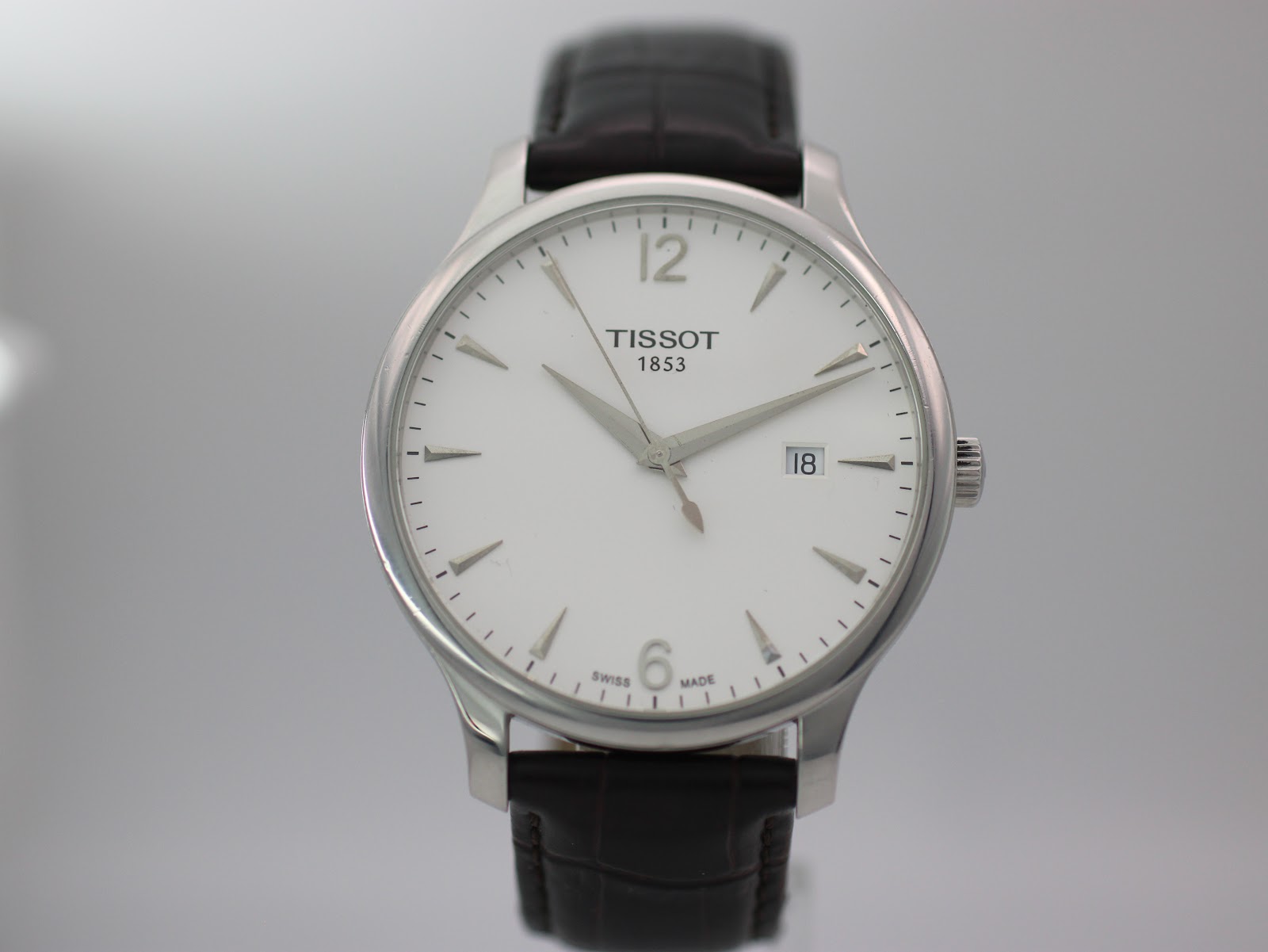 Front view of the Tissot T063610 A watch, showcasing its crisp white dial, silver-tone baton indices, and Arabic numerals at 12 and 6 o'clock.