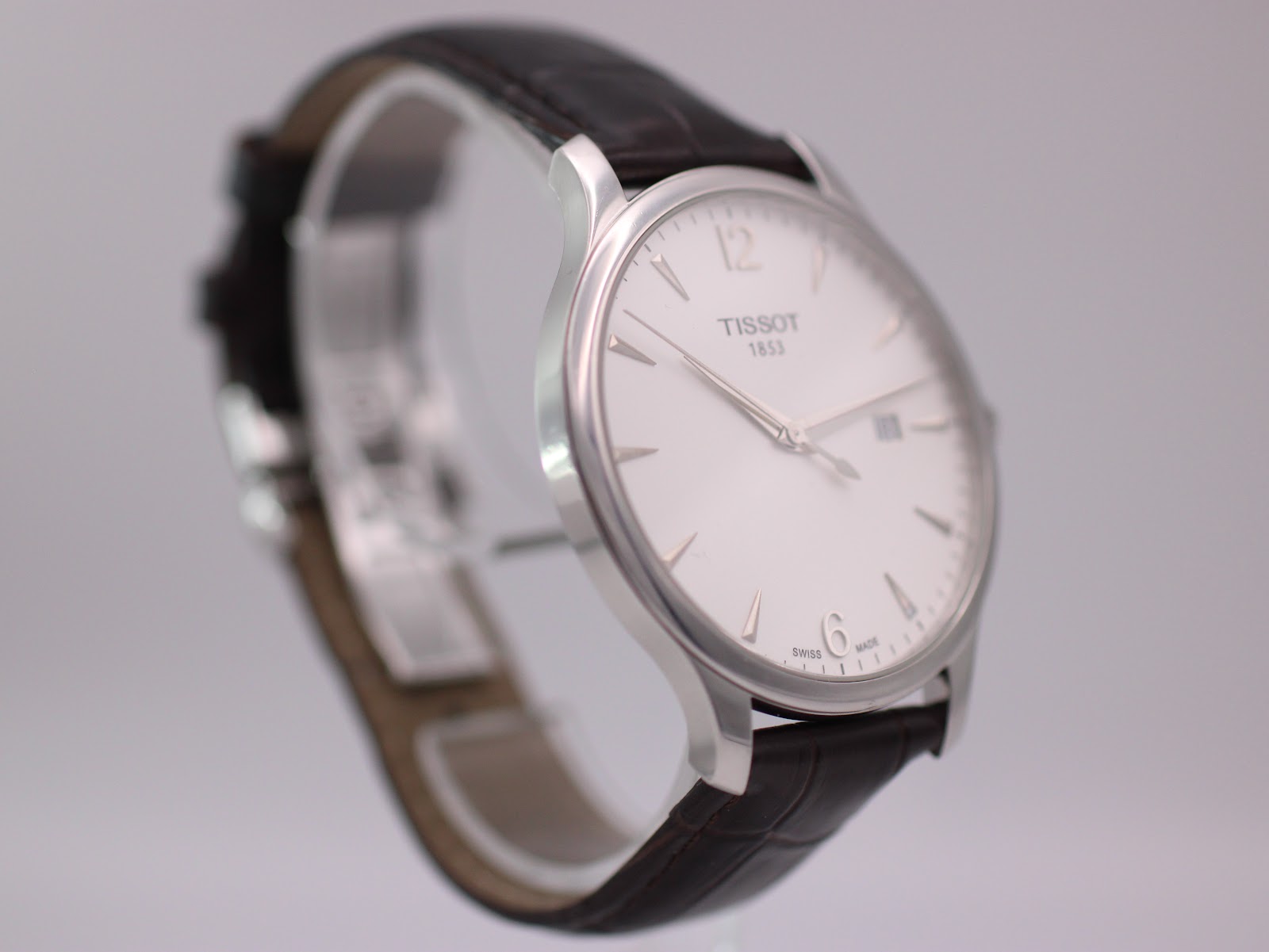 Angled view of the Tissot T063610 A watch, showcasing the clean white dial, slim profile, and brown leather strap.