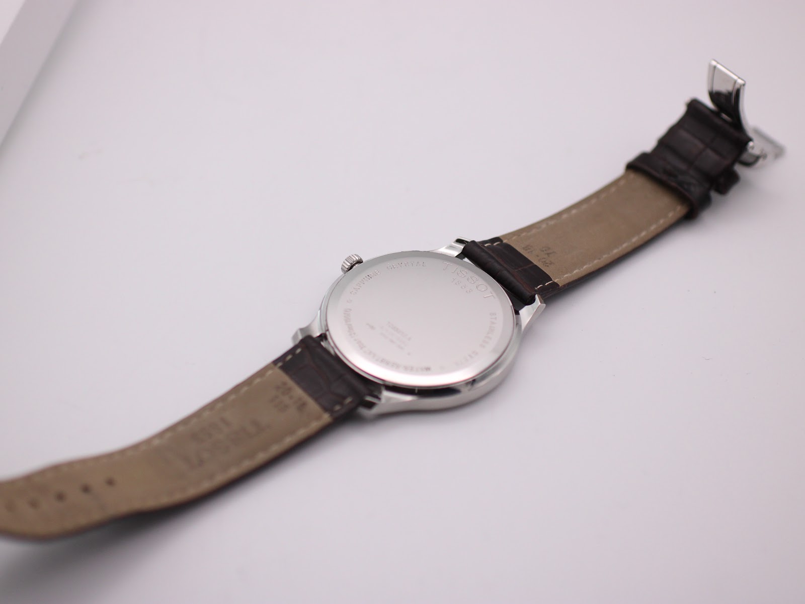 Rear view of the watch, showing the stainless steel case back with engravings, and the extended brown leather strap.