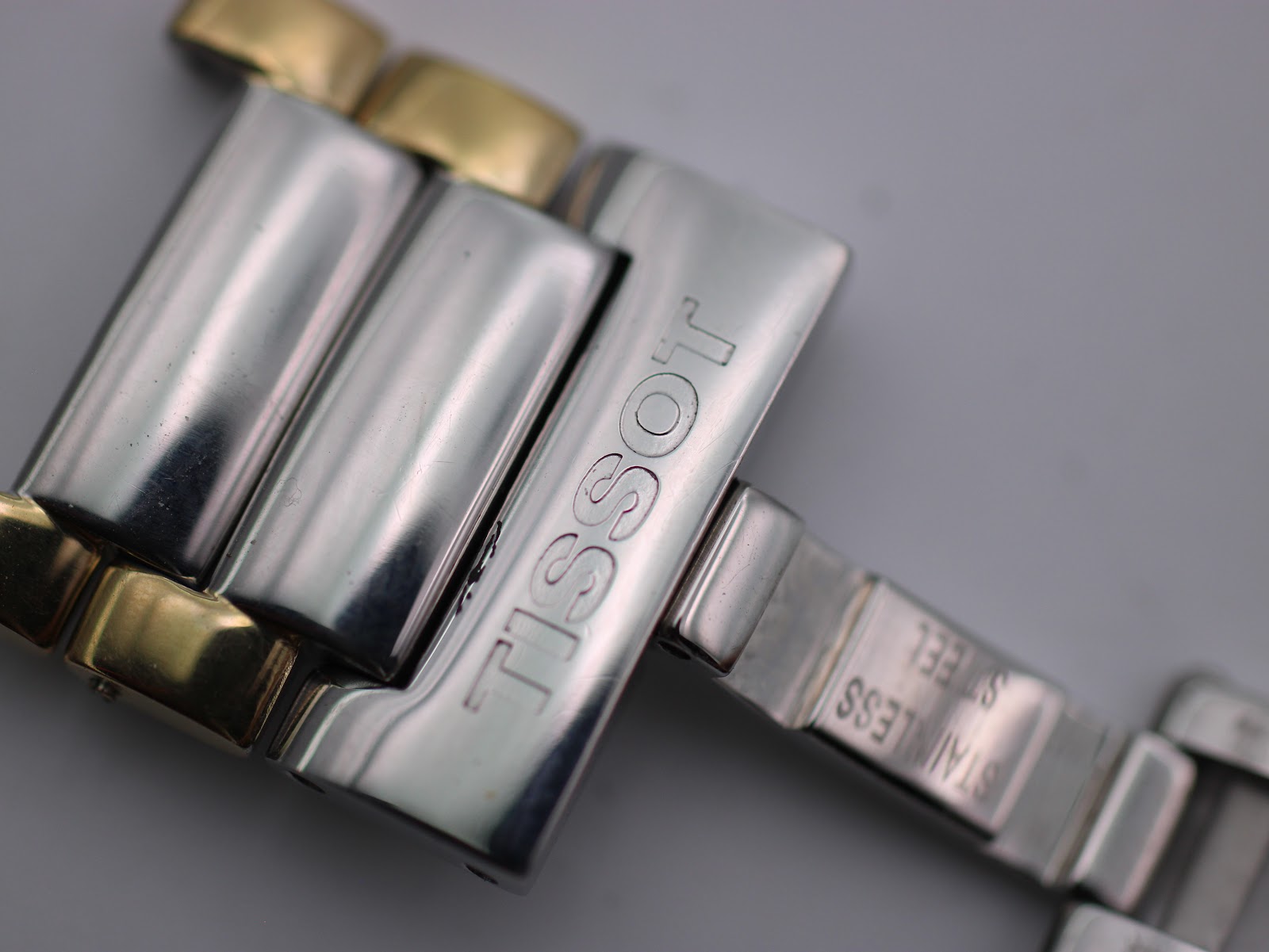 Close-up of the signed Tissot butterfly clasp on the two-tone stainless steel bracelet.