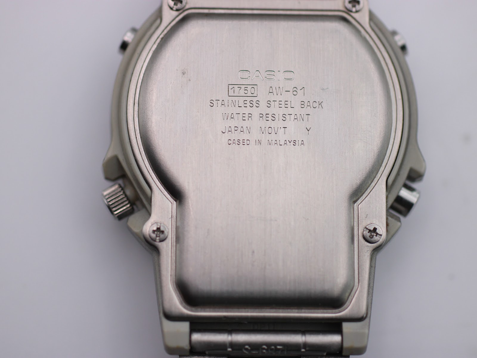 Close-up of the brushed stainless steel case back of the Casio AW-61, showing model number and manufacturing information.