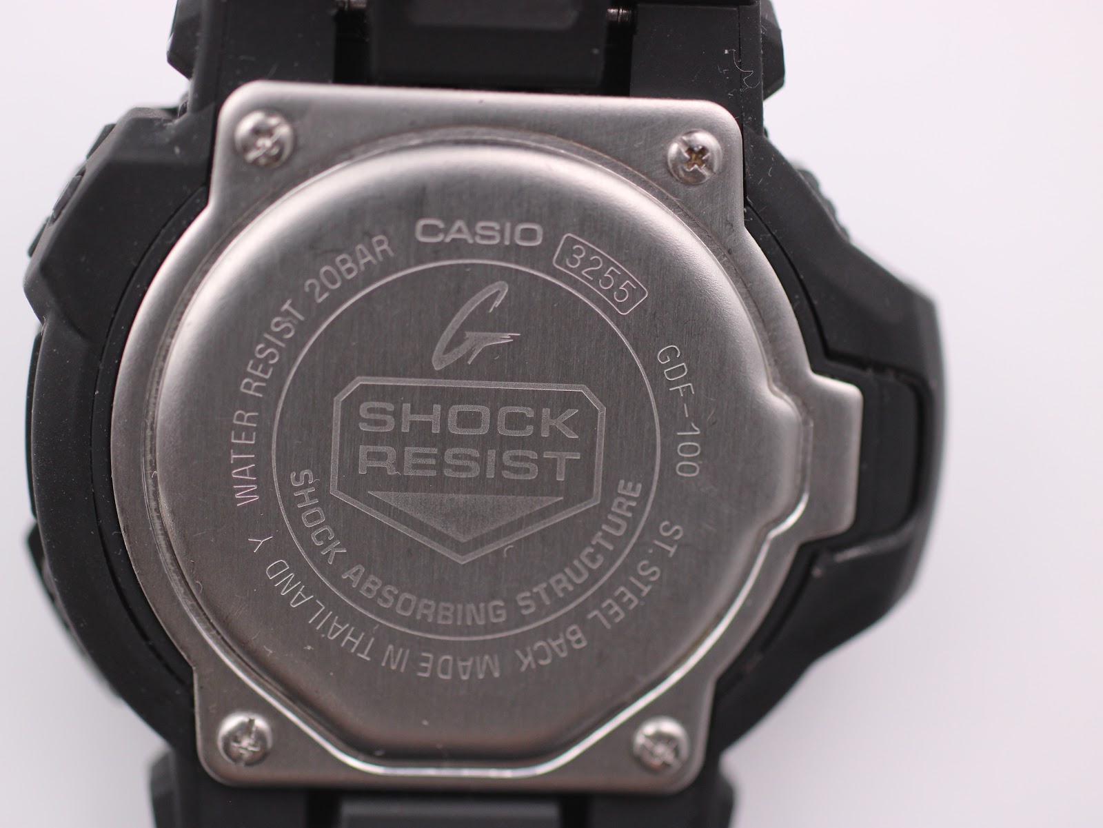 Close-up of the stainless steel case back of the Casio G-Shock GDF-100, showing "GDF-100", "WATER RESIST 20BAR", and "SHOCK RESIST" engravings.
