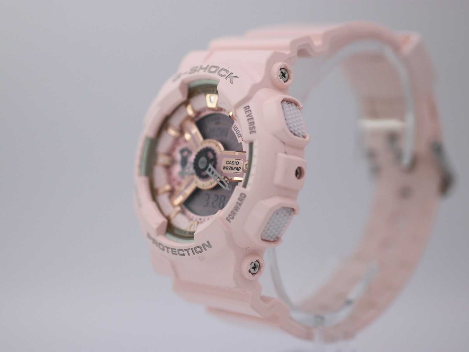 Right-side profile view of the pink G-SHOCK watch showing buttons and case texture on a clear stand.