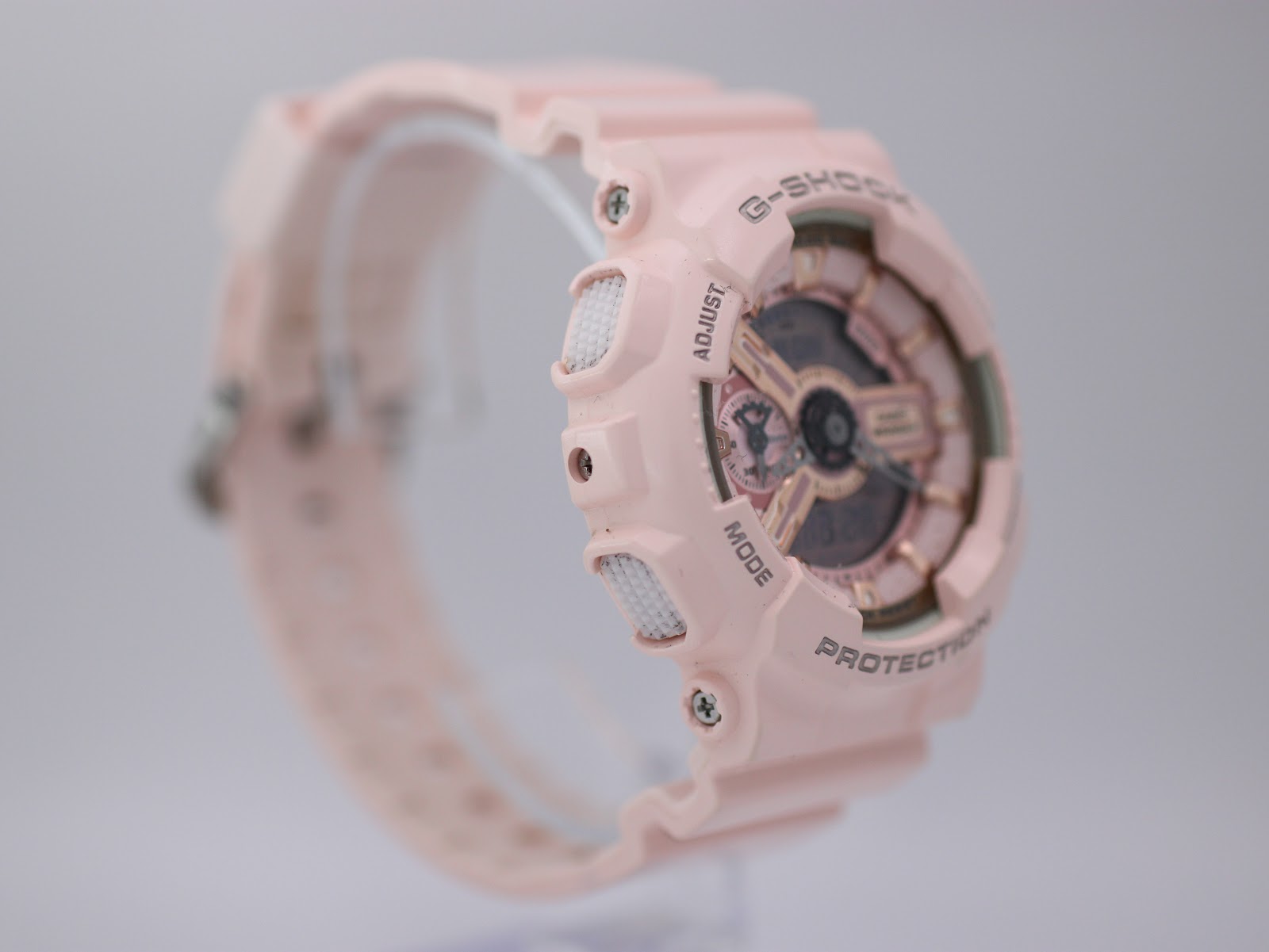 Left-side profile view of the pink G-SHOCK watch showing "MODE" and "ADJUST" buttons.