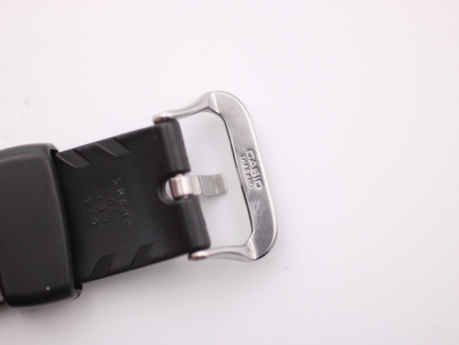 Close-up of the stainless steel buckle, engraved with 'CASIO THAILAND', and the end of the black rubber strap.