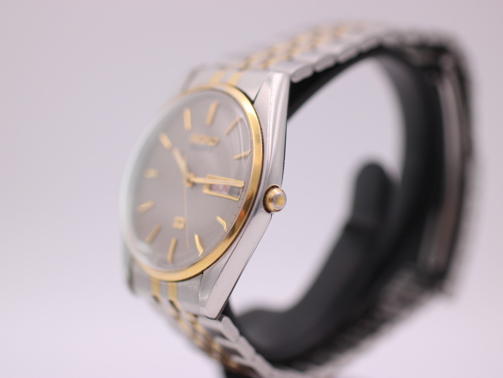 Side profile view of the Seiko quartz watch on a display stand, showing the gold-tone crown and case.