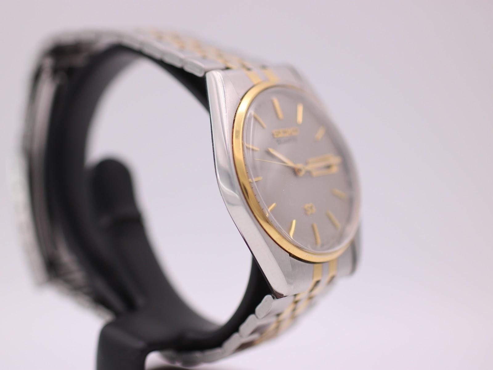 Angled side view of the Seiko two-tone watch, highlighting the gold-tone bezel and bracelet links on a stand.