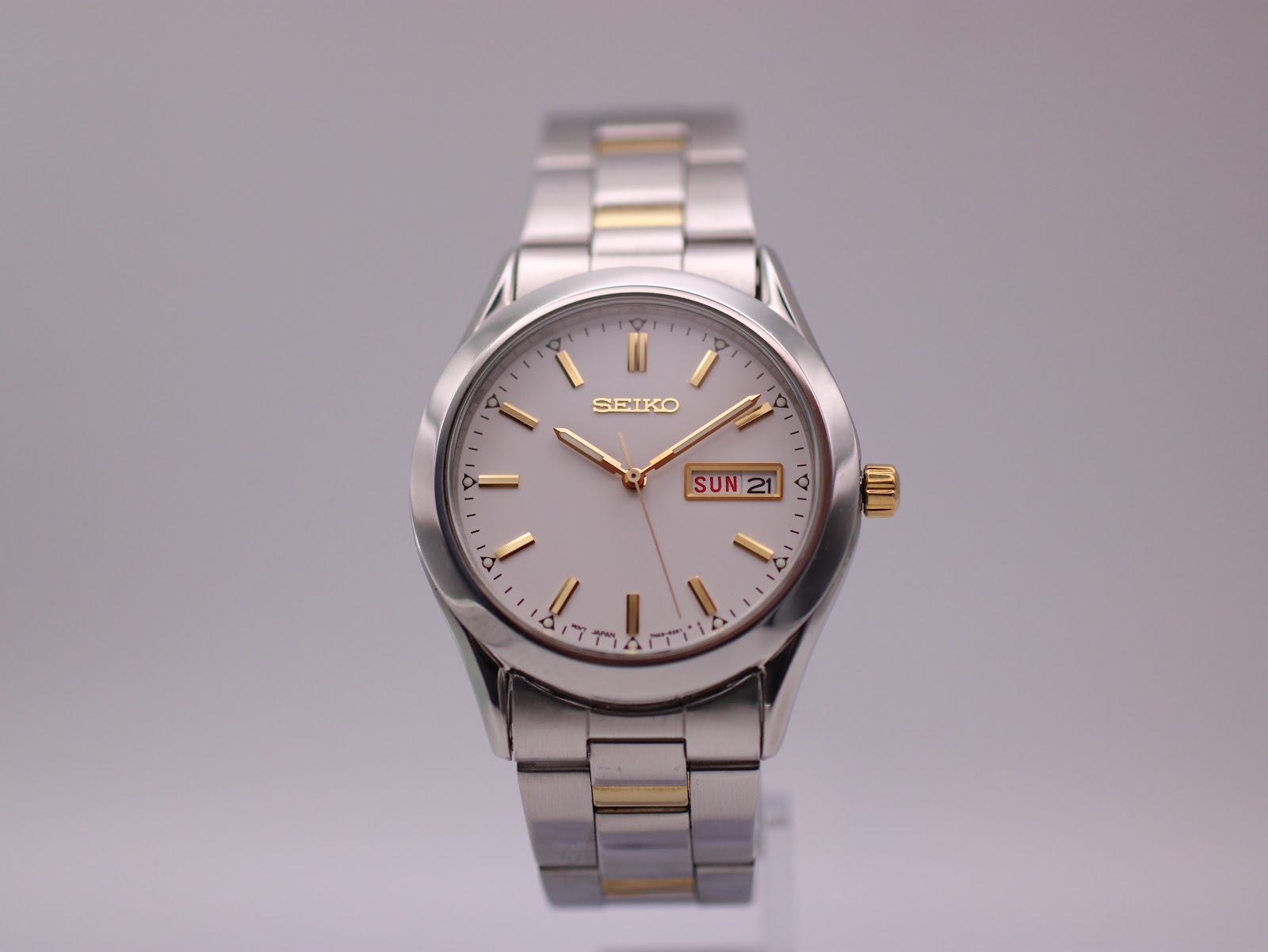 Front view of the Seiko 7N43-9070 watch with white dial, gold baton indices, and two-tone stainless steel bracelet on a grey background.