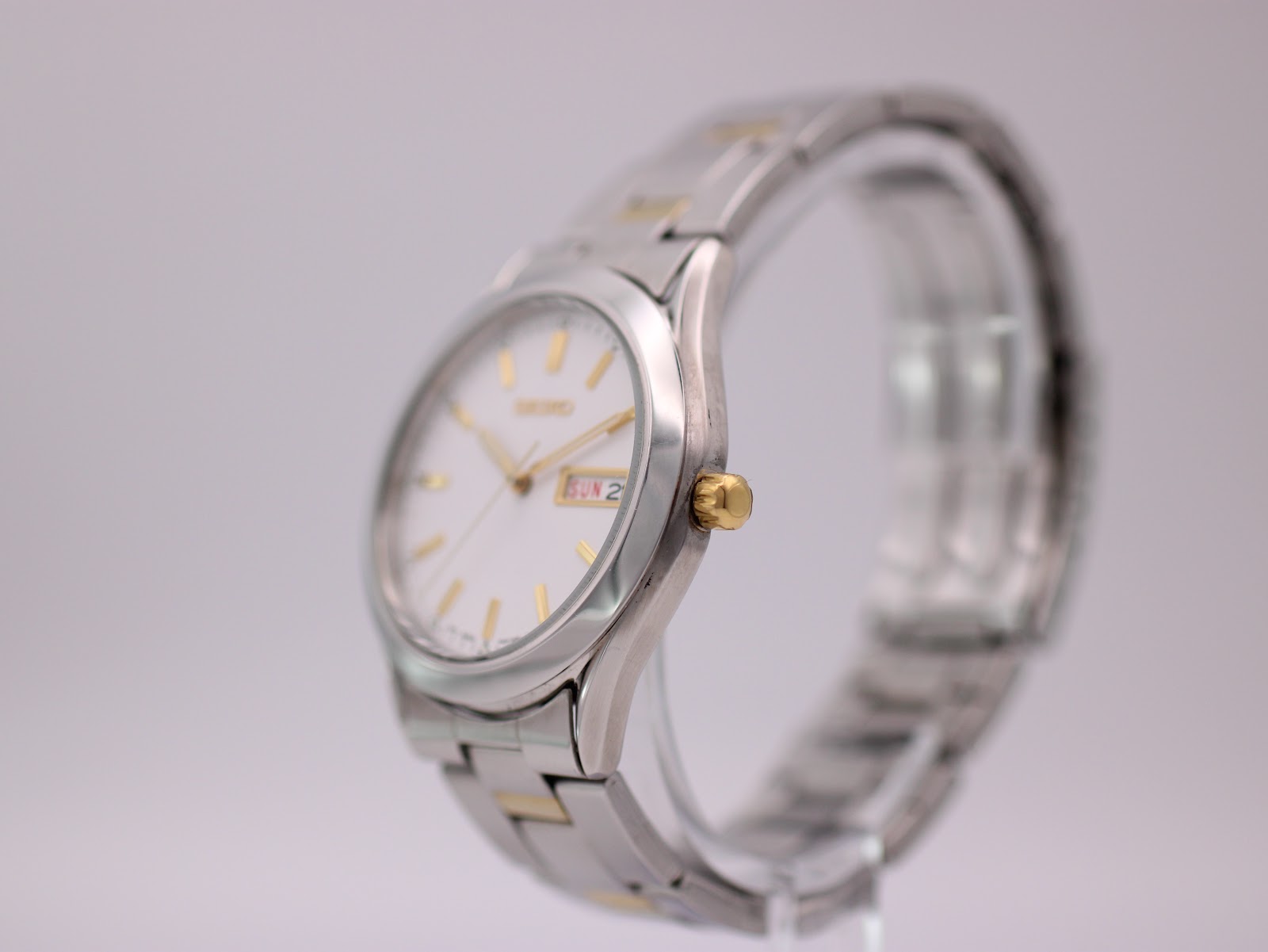 Side profile view of the Seiko watch, showing the gold-tone crown and the curvature of the silver-tone case and two-tone bracelet.