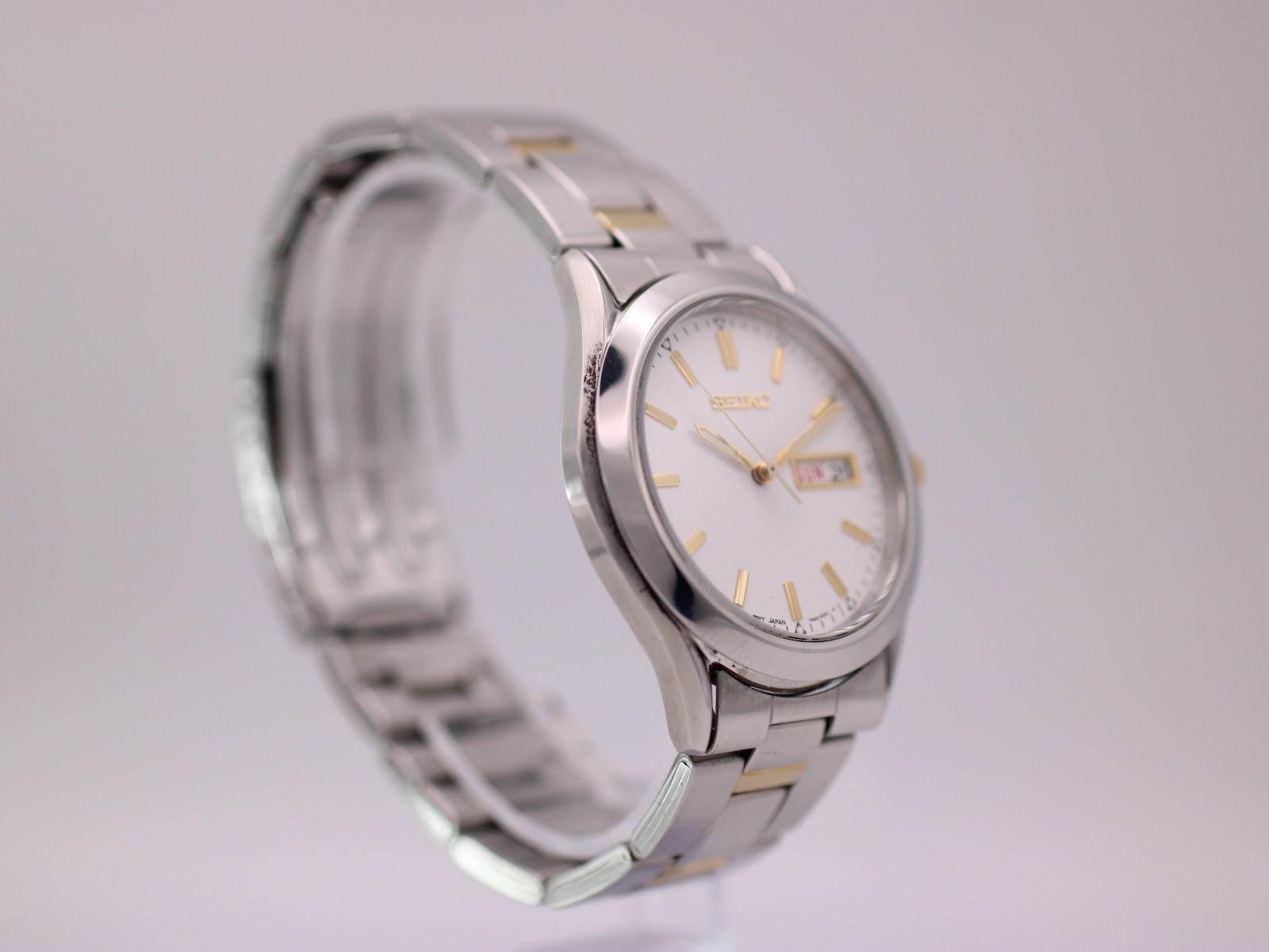 Angled side view of the Seiko watch, highlighting the silver case, gold crown, and the alternating gold and silver links of the bracelet.