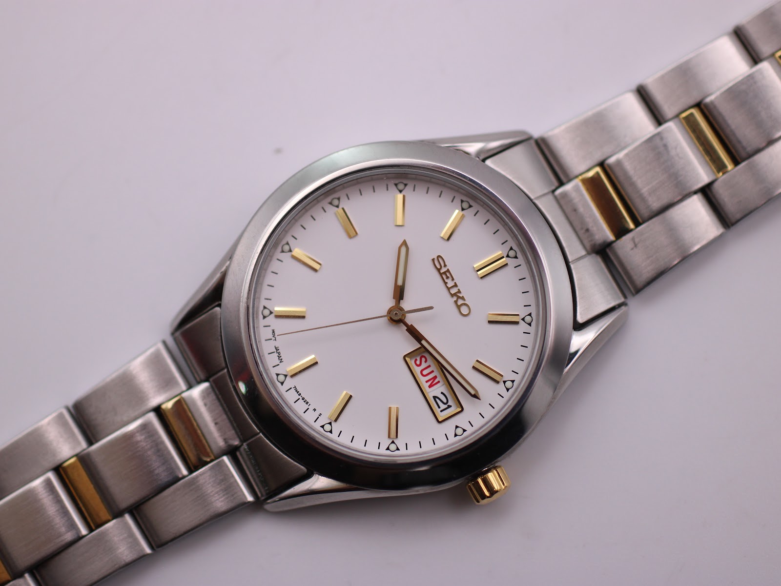 Close-up, top-down view of the Seiko dial and two-tone bracelet, showing the day-date window and the polished gold-tone hour markers.
