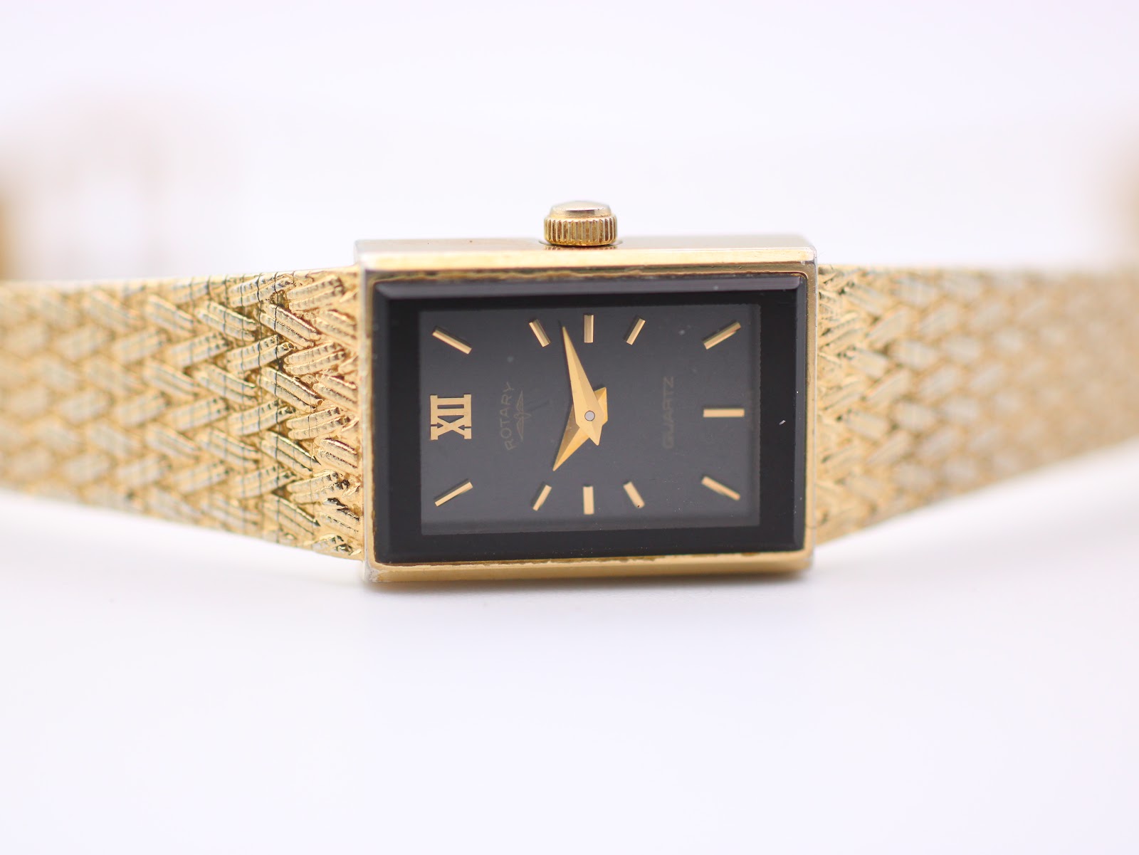 Opposite angled side view of the Rotary watch, highlighting the case profile and bracelet texture on a clear stand.