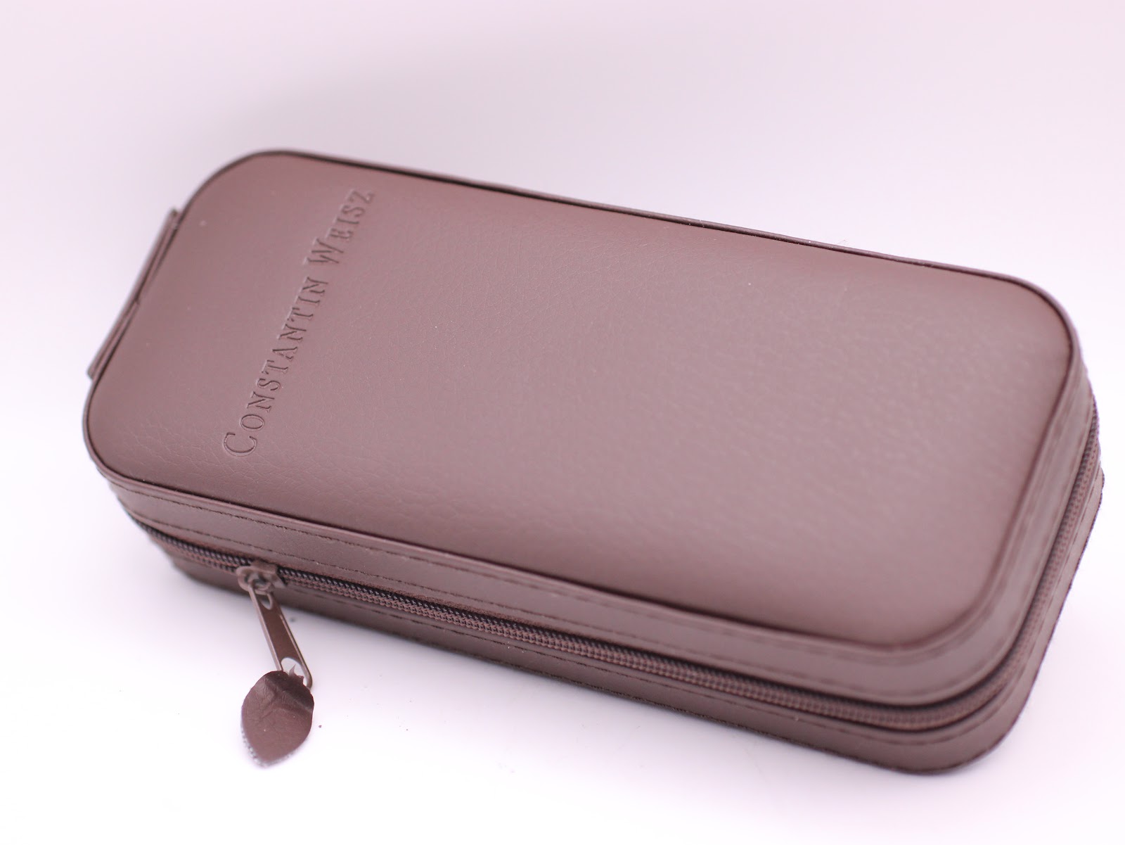 Closed view of the brown Constantin Weisz branded zipped travel case, made of leatherette material.