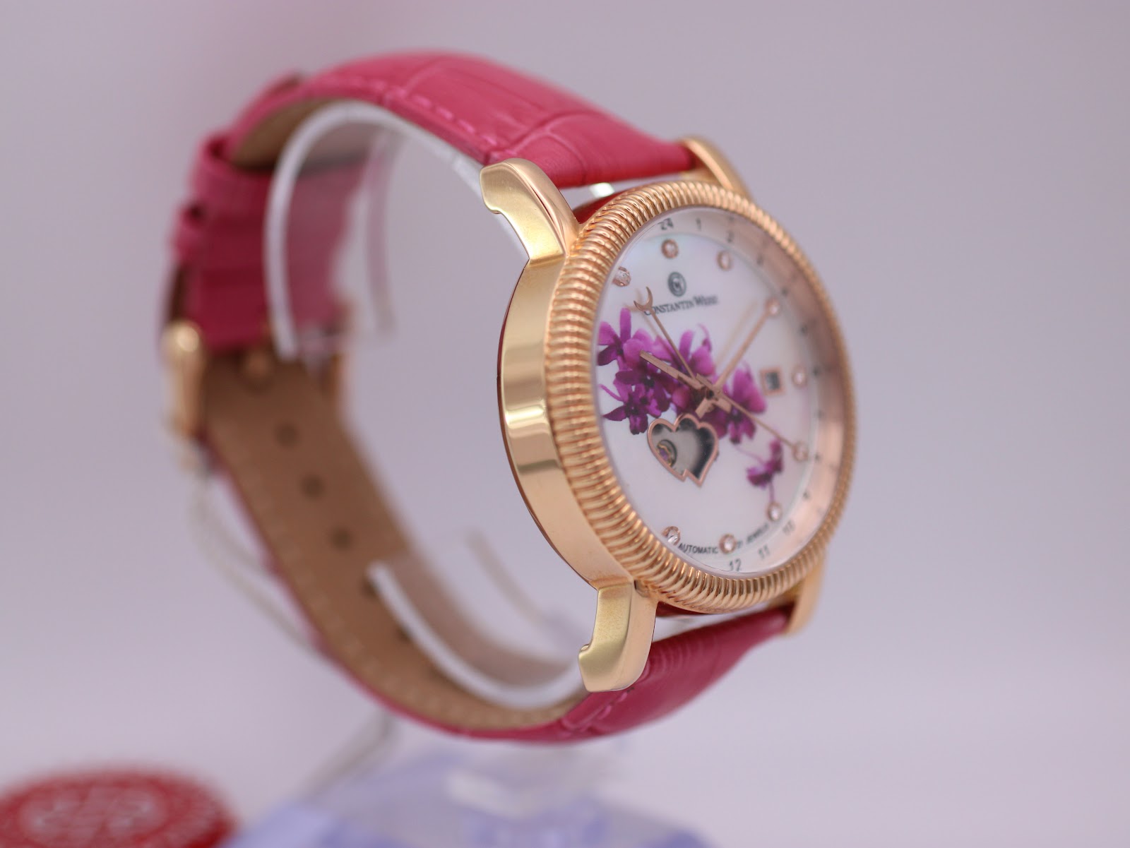 Another angled side view of the watch on display, focusing on the polished rose gold tone case, the intricate fluted detailing on the bezel, and the curved lugs.