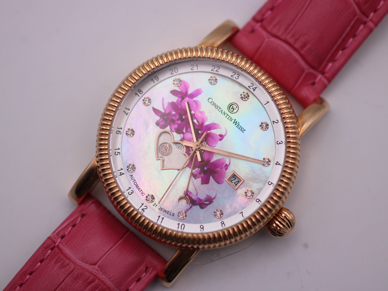 Top-down close-up of the Constantin Weisz watch dial, showcasing the detailed pink and purple floral pattern, the open-heart complication, the date window, and the outer 24-hour track with crystal markers.
